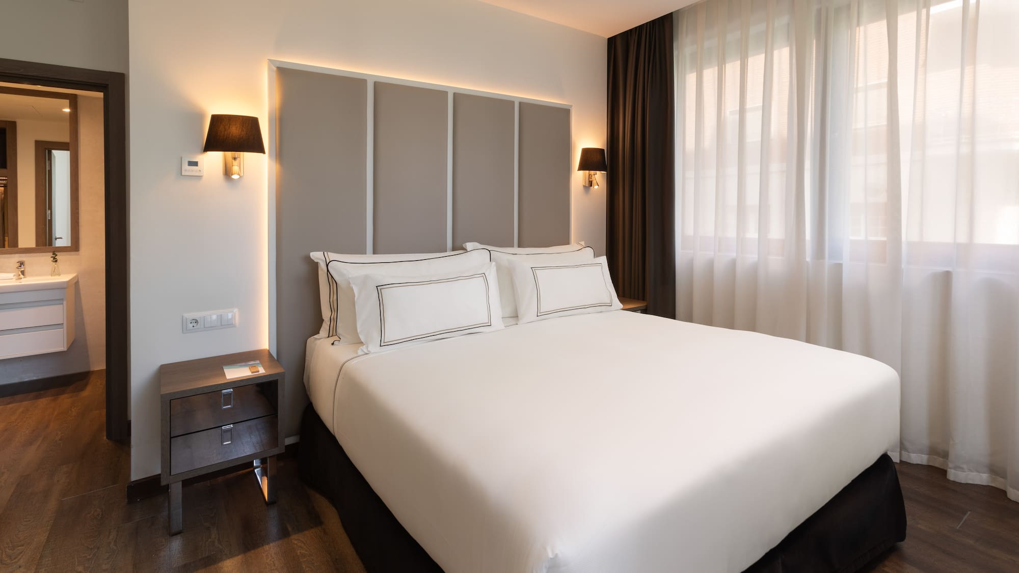 Habitación de hotel moderna con cama doble, cabecero iluminado y baño.