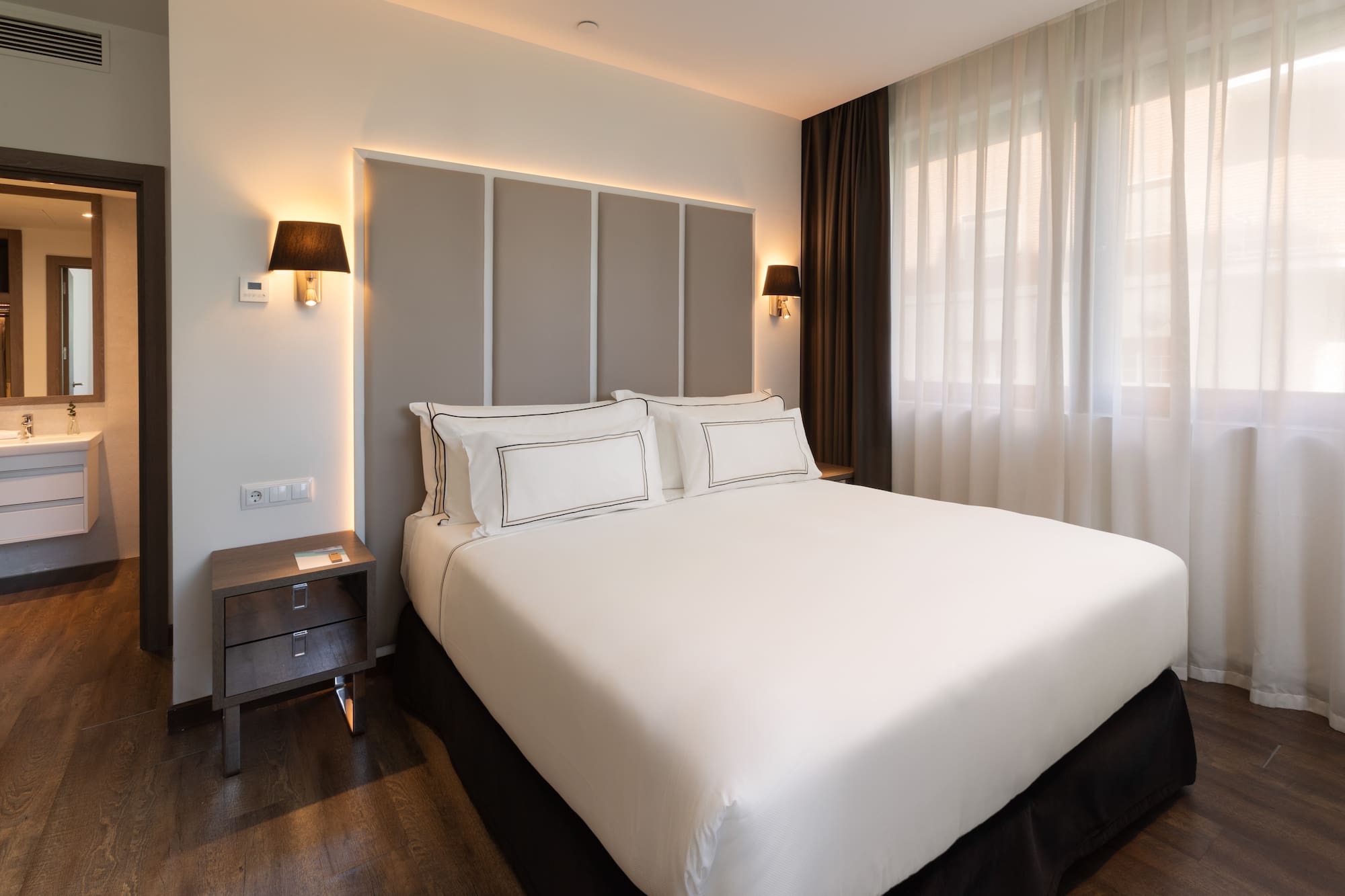 Habitación de hotel moderna con cama doble, cabecero iluminado y baño.