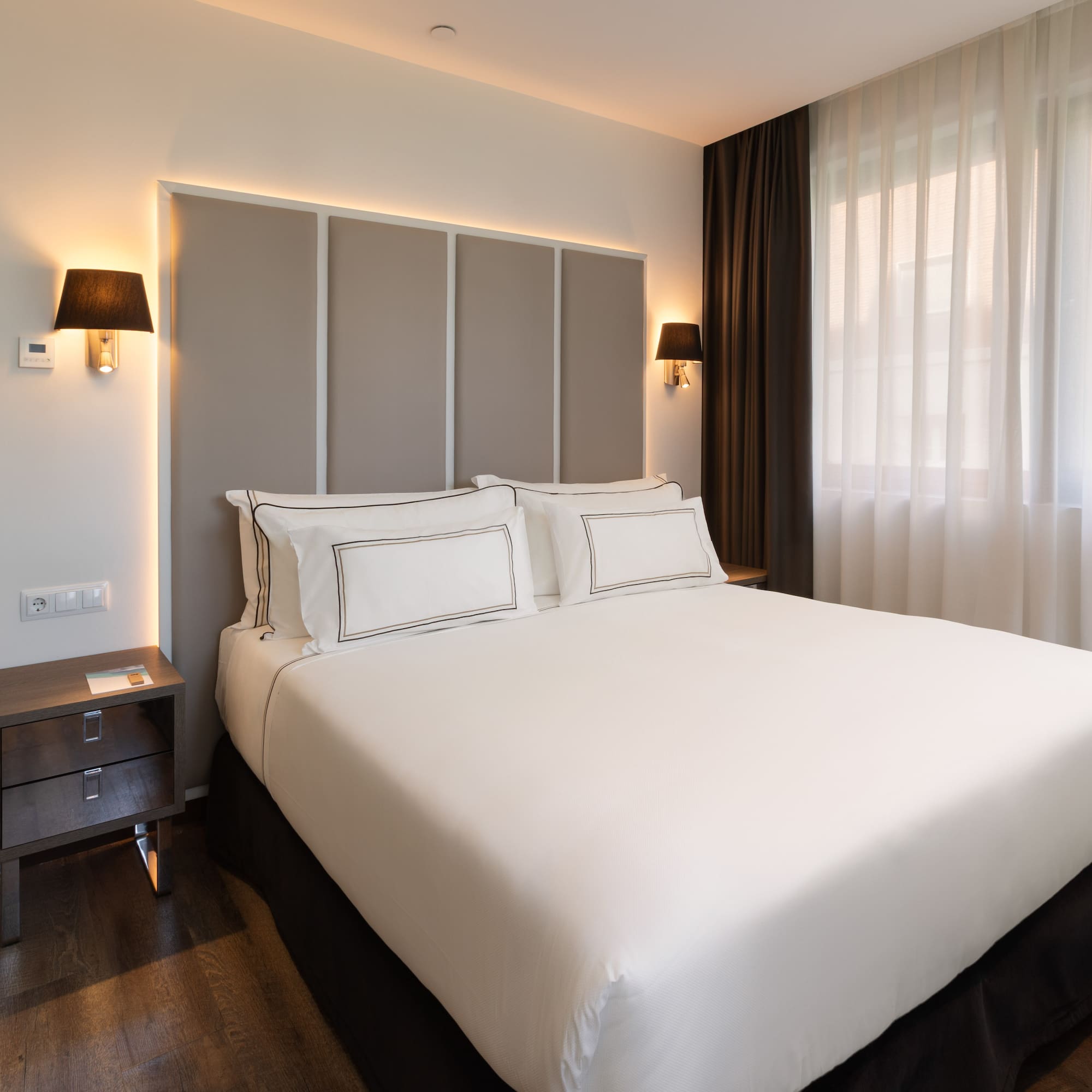 Habitación de hotel moderna con cama doble, cabecero iluminado y baño.