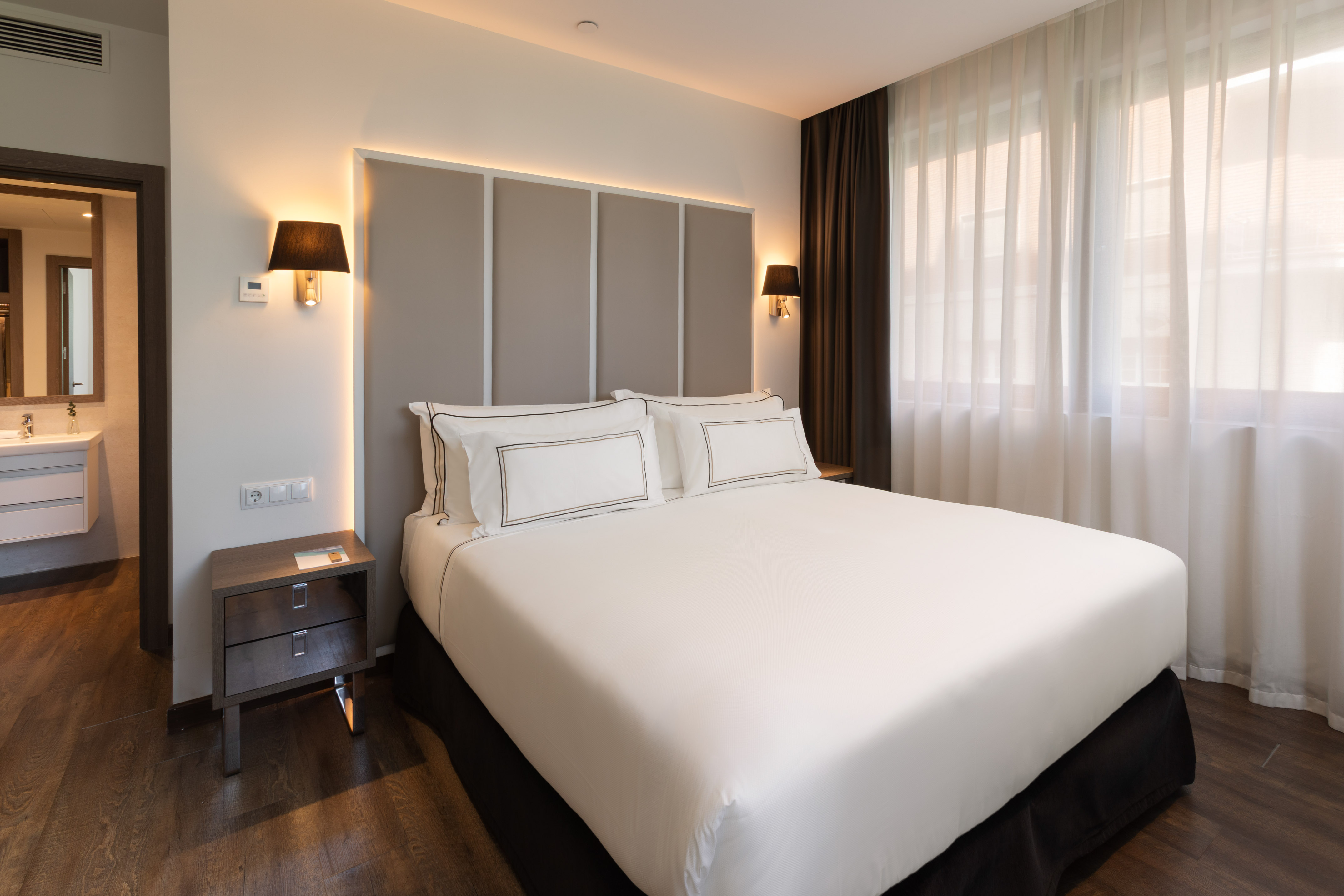 Habitación de hotel moderna con cama doble, cabecero iluminado y baño.