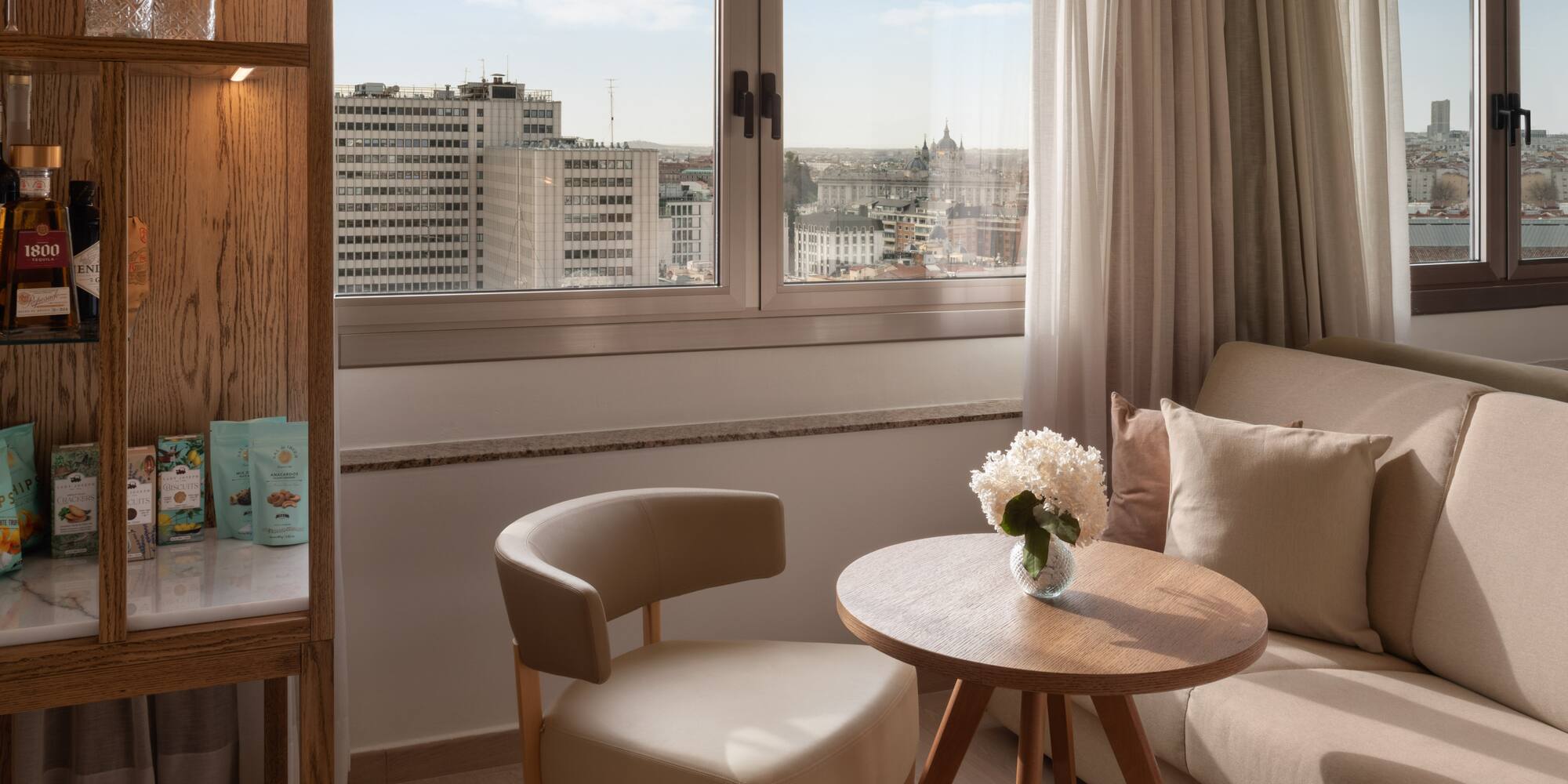 Luxury hotel room in Madrid with city view, comfortable seating, and minibar.