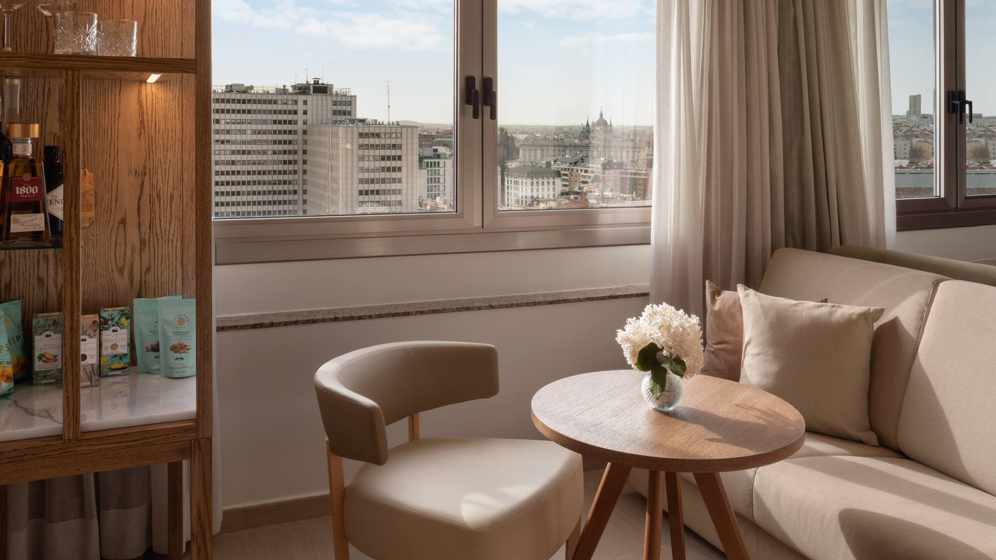 Luxury hotel room in Madrid with city view, comfortable seating, and minibar.