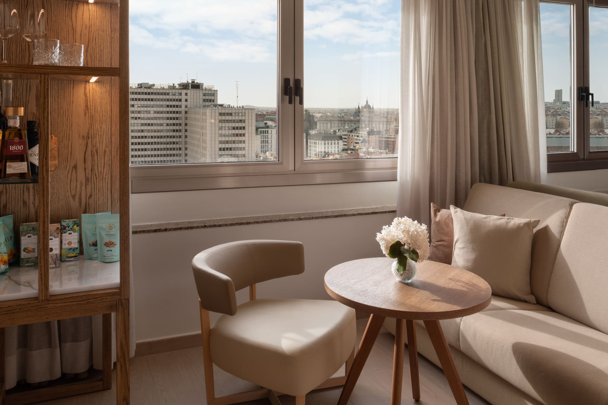 Luxury hotel room in Madrid with city view, comfortable seating, and minibar.