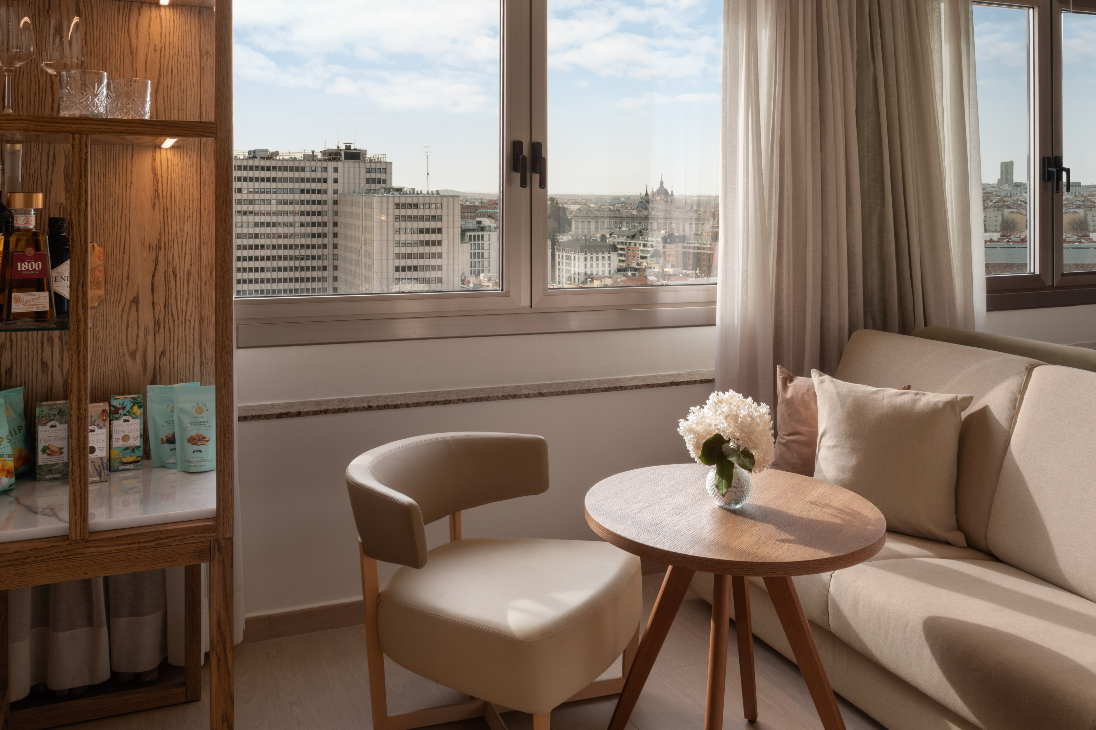 Modern hotel suite, Madrid city view, lounge area, and wooden mini-bar.
