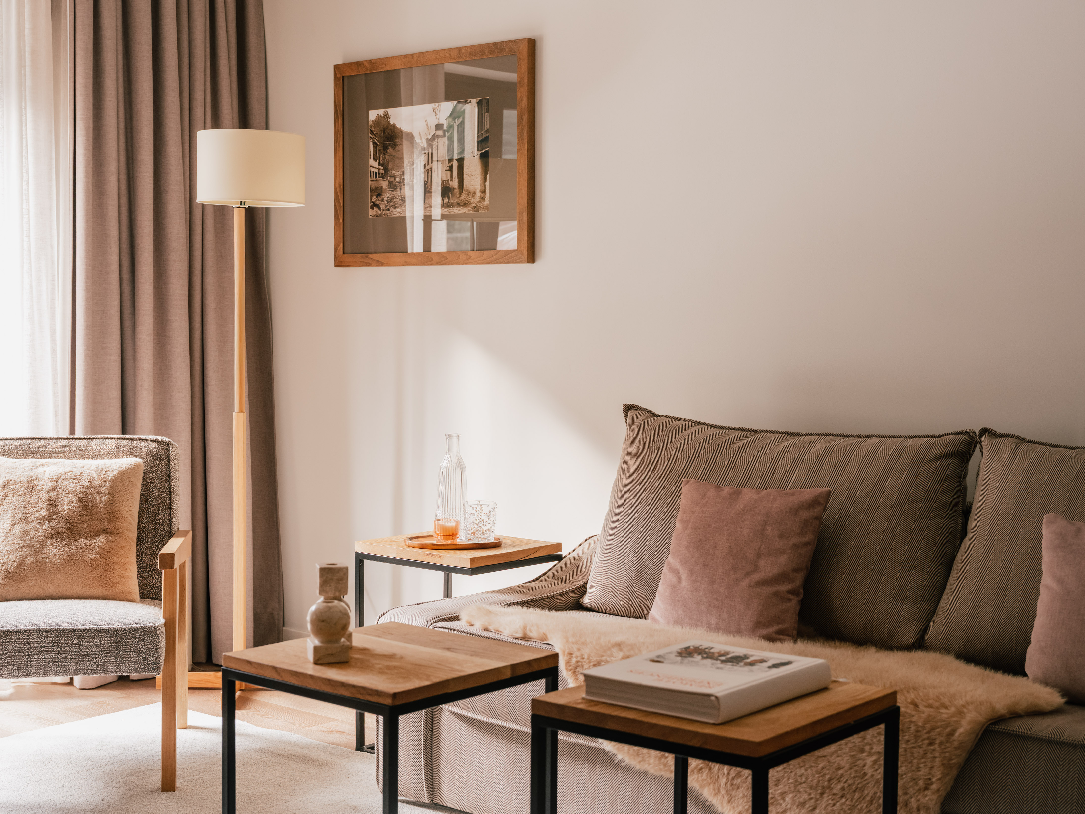 Neutral living room interior with cozy sofa, wooden tables, and floor lamp.
