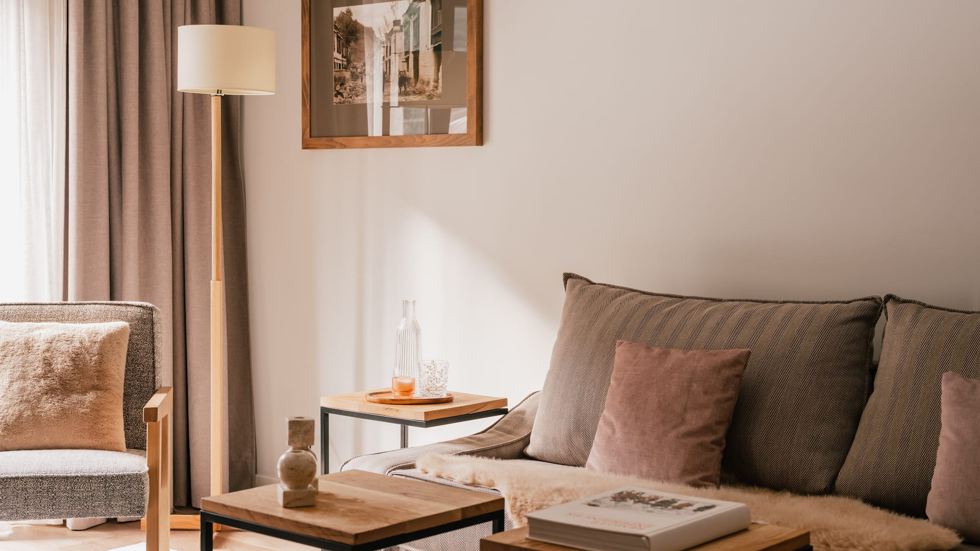 Neutral living room interior with cozy sofa, wooden tables, and floor lamp.