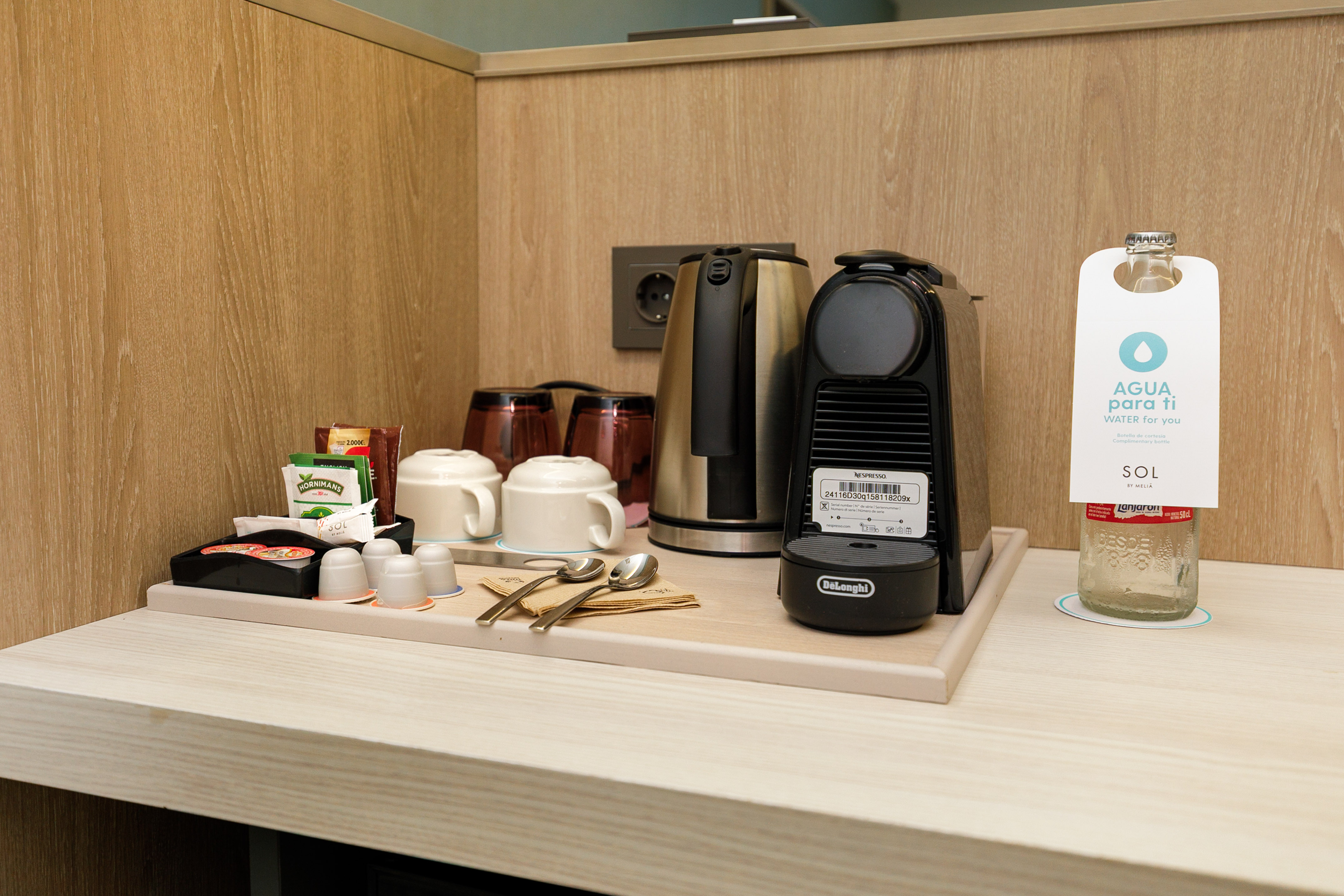 Hotel room coffee station with Nespresso, kettle, tea, mugs, bottled water.