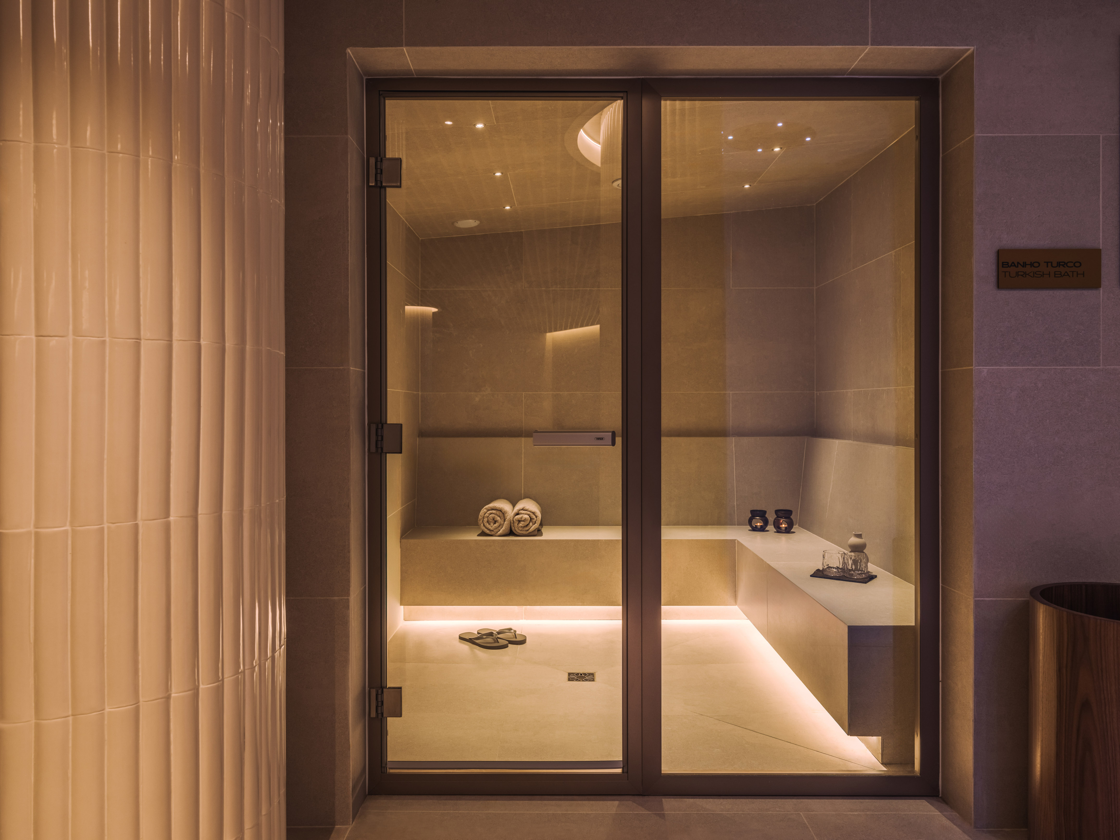 Modern Turkish bath with glass door, stone benches, and warm lighting.