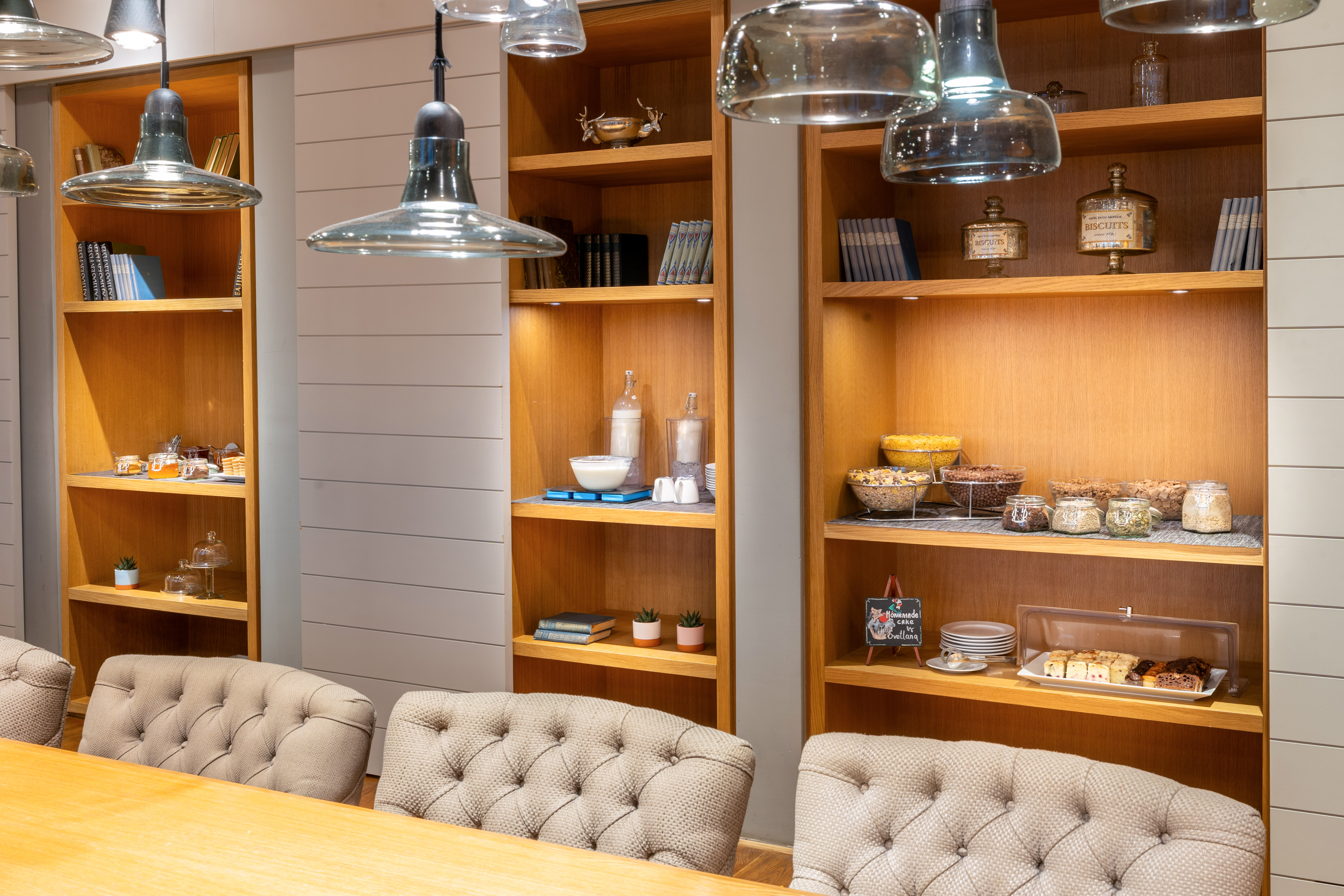 Breakfast buffet on wooden shelves, cereals, pastries, modern pendant lights.