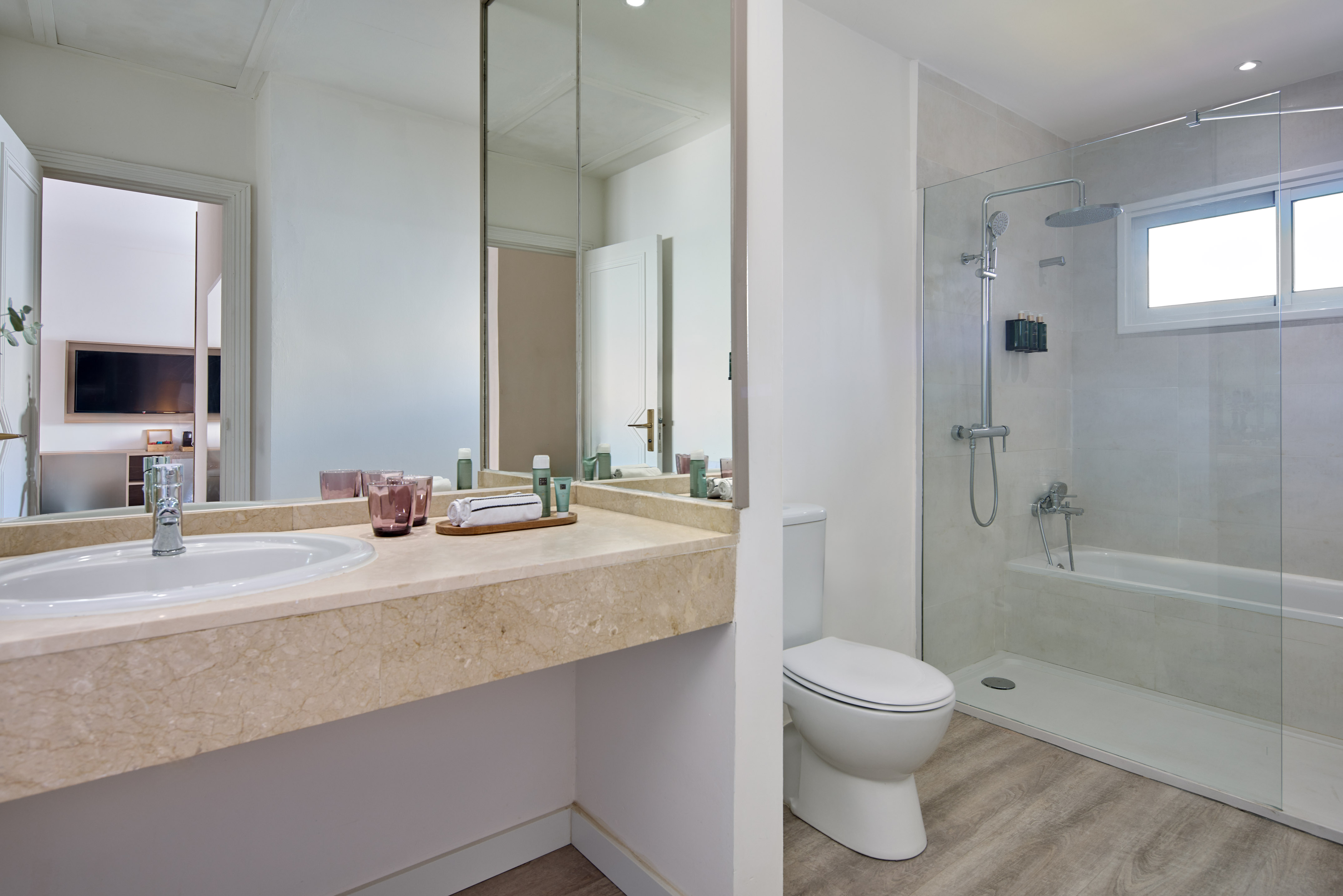 Modern bathroom with marble vanity, mirror, toilet, and glass shower-tub combo.