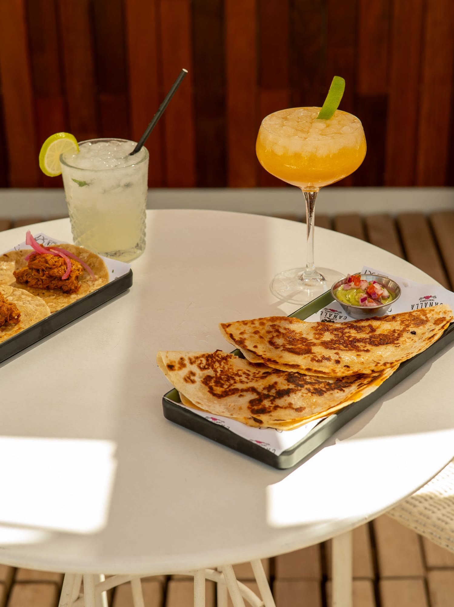Mexican tacos, quesadillas, cocktails, and guacamole on a white outdoor table.