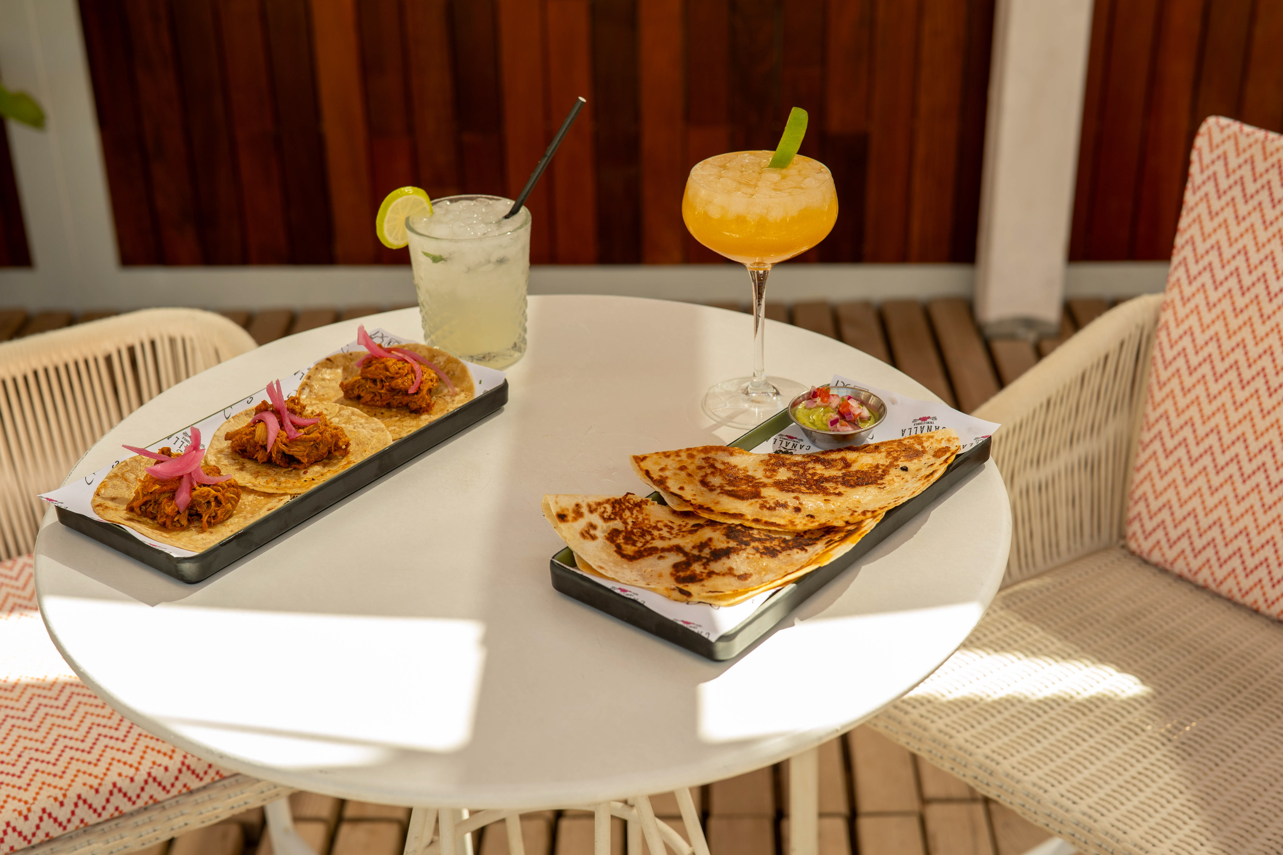 Mexican tacos, quesadillas, cocktails, and guacamole on a white outdoor table.
