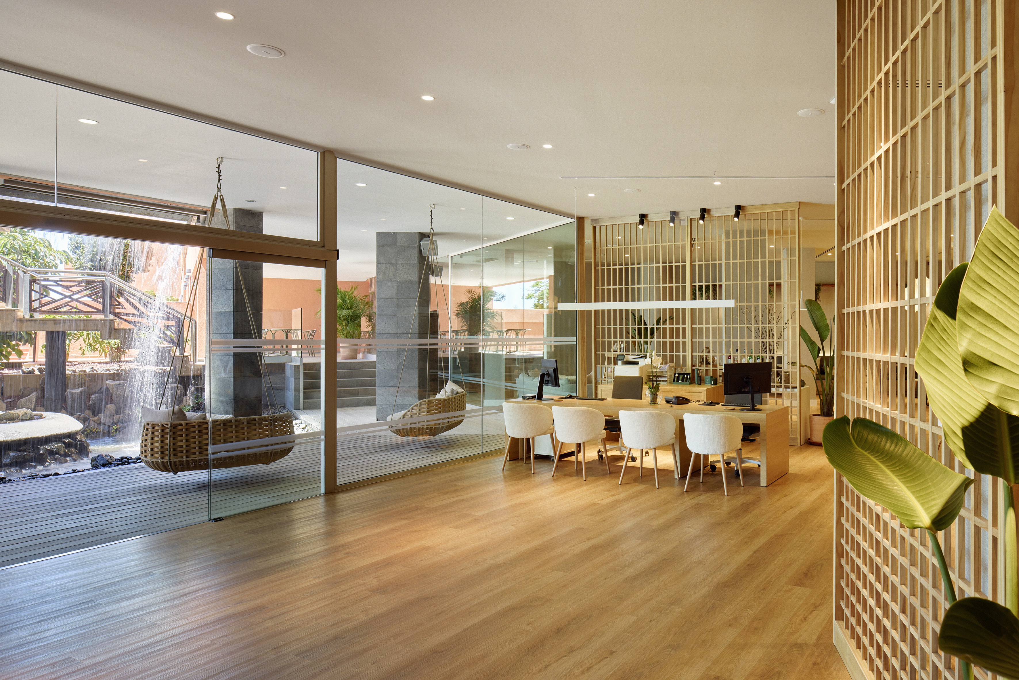 Modern hotel reception with glass wall overlooking waterfall and suspended swing chair.