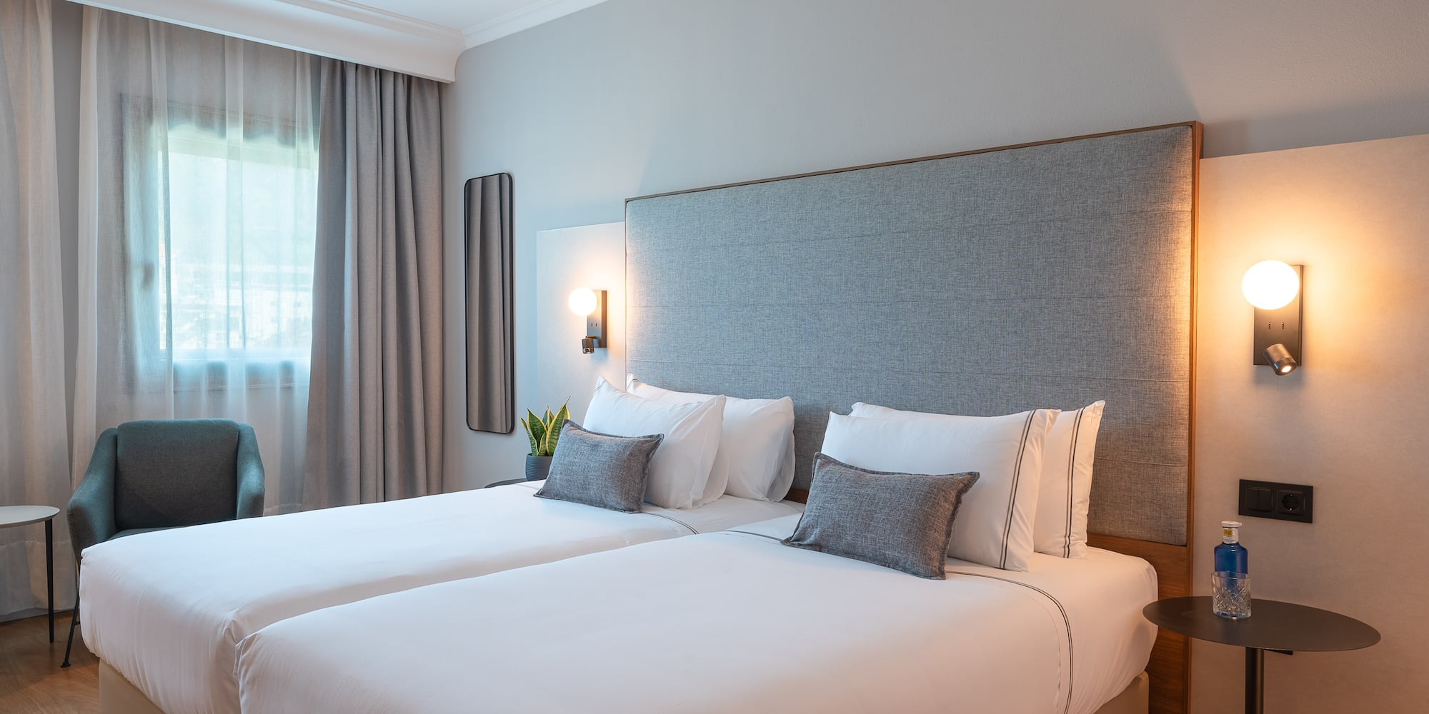Habitación doble de hotel moderna con camas individuales y cabecero gris.