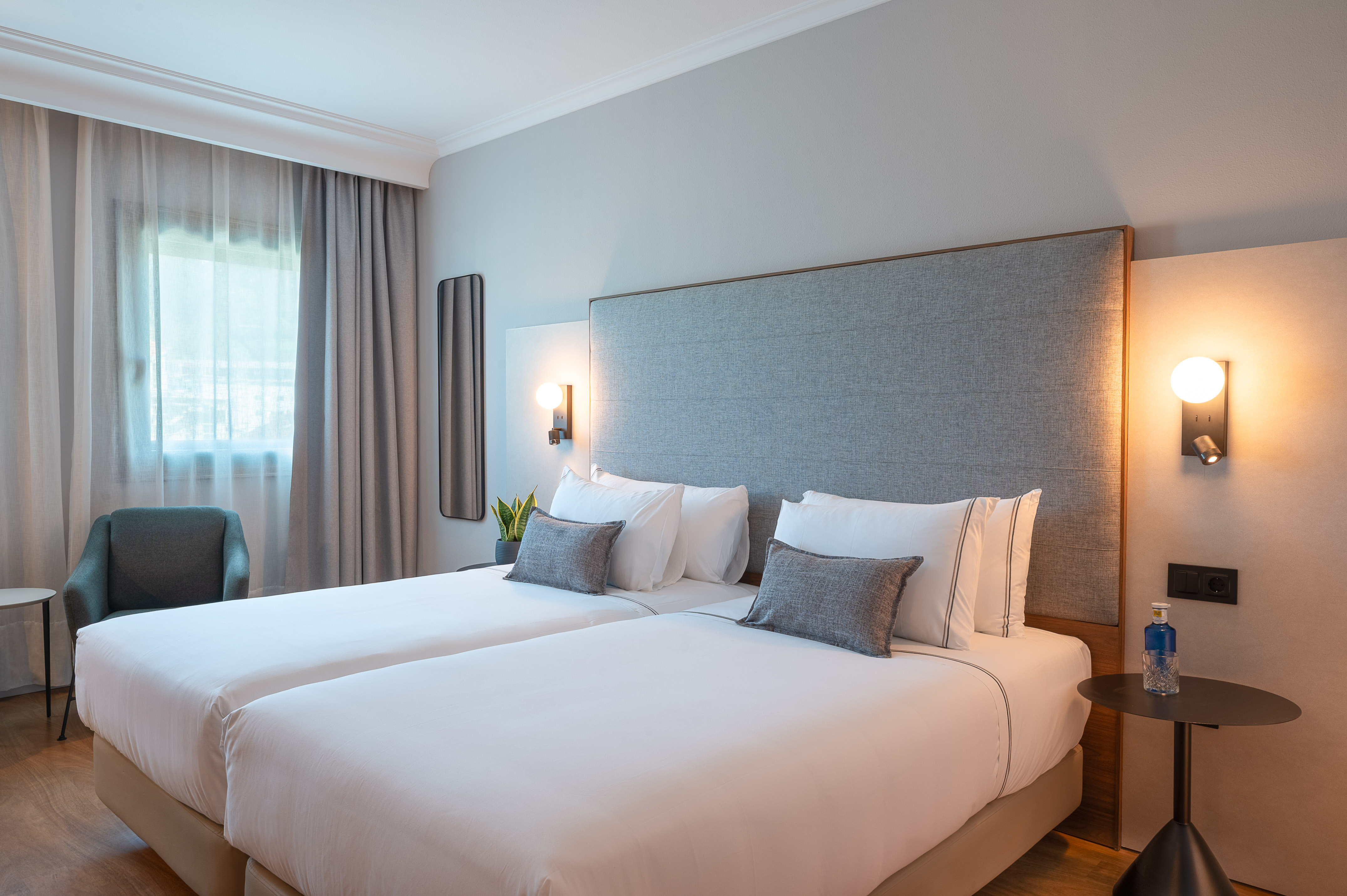 Habitación doble de hotel moderna con camas individuales y cabecero gris.