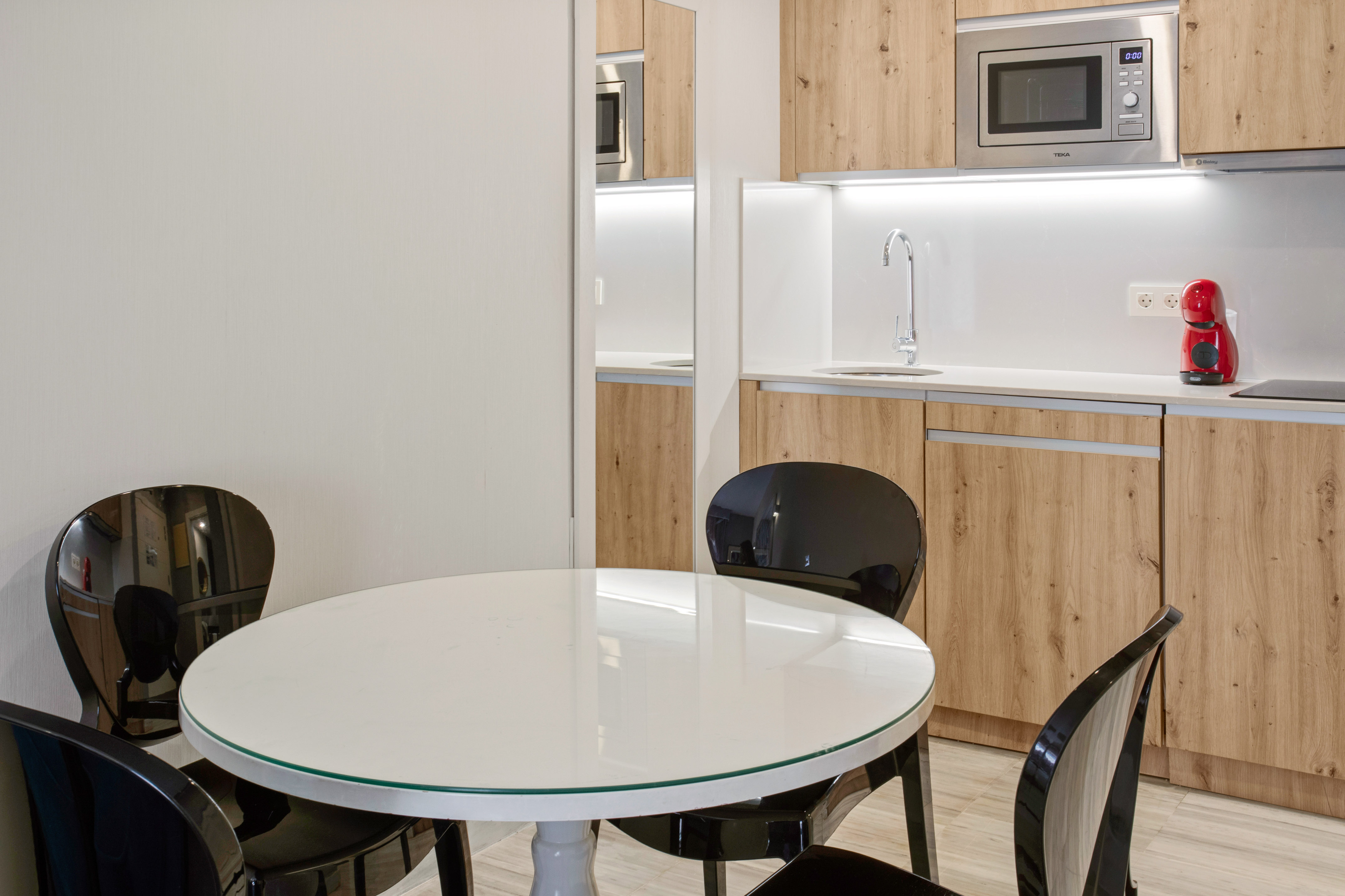 Compact modern kitchen with wood cabinets, white table, and black chairs.
