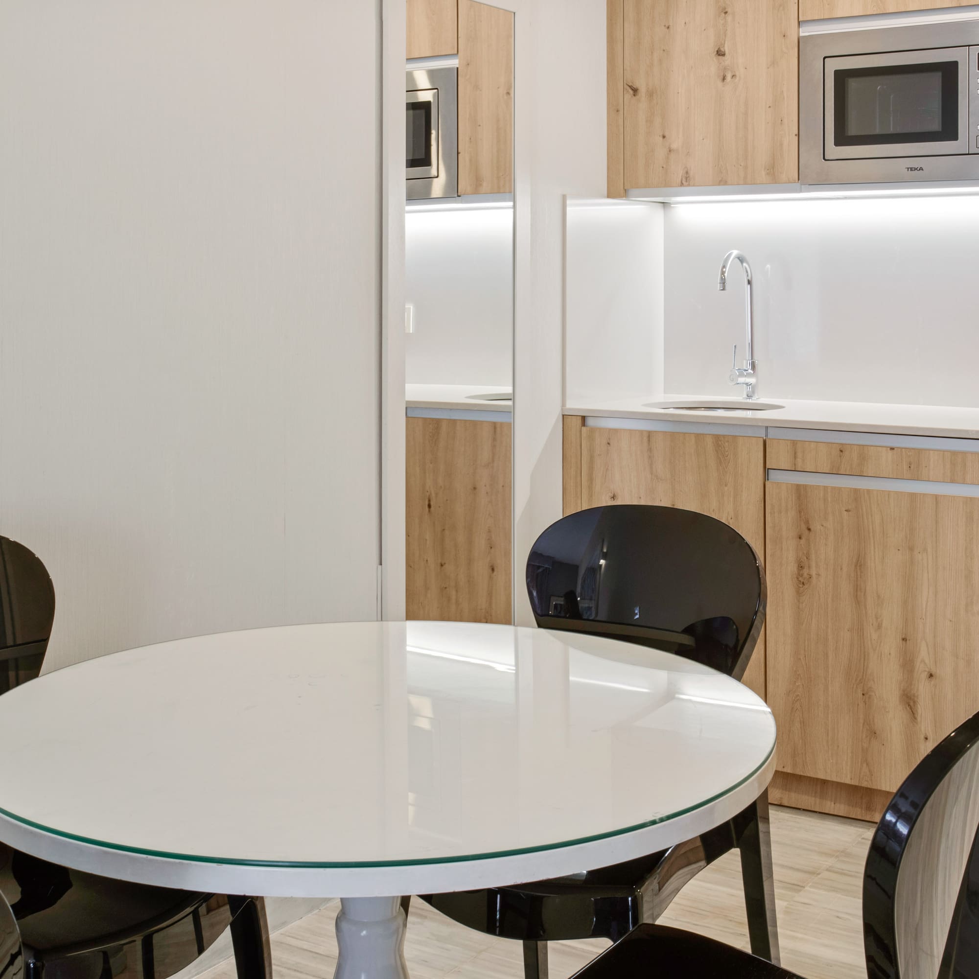 Compact modern kitchen with wood cabinets, white table, and black chairs.