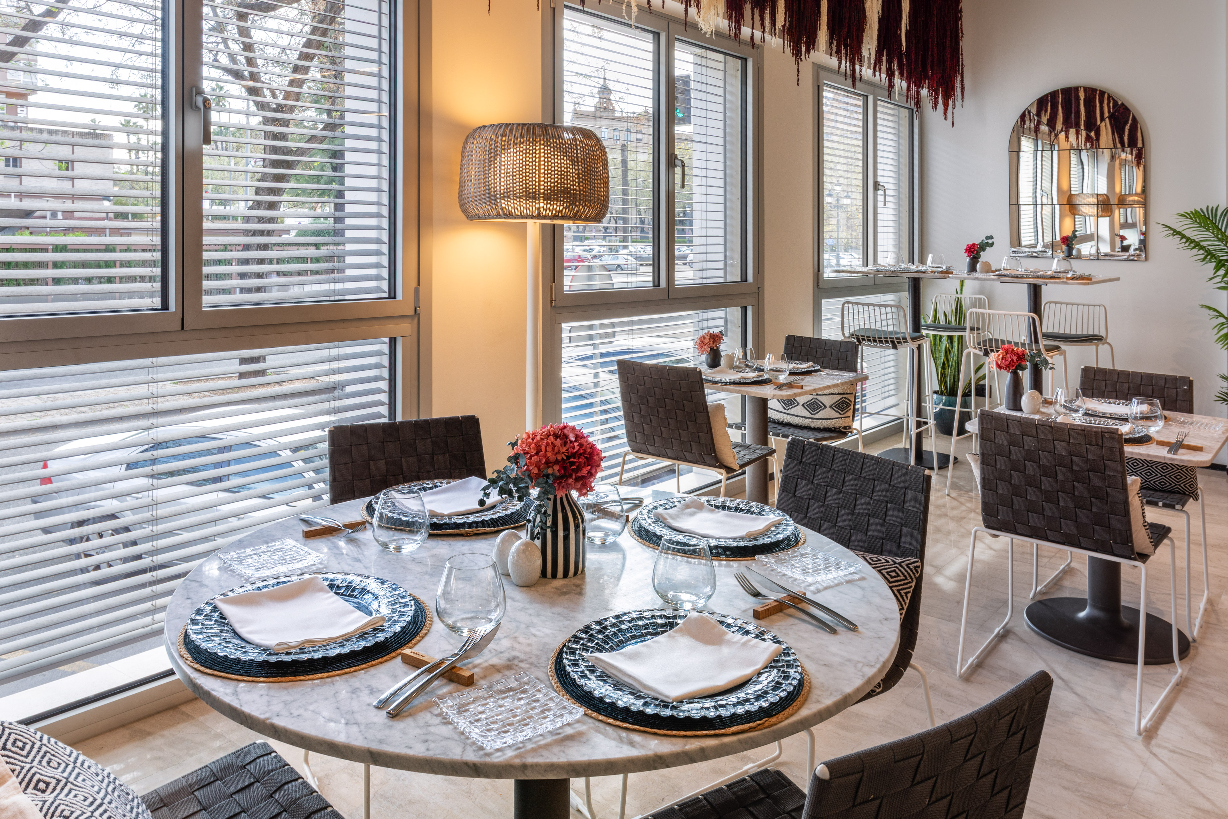 Bright modern restaurant dining room with marble tables, woven chairs, window views.
