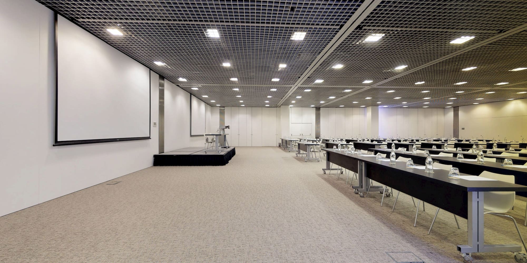 Modern conference room with stage, screen, and rows of tables for meetings.
