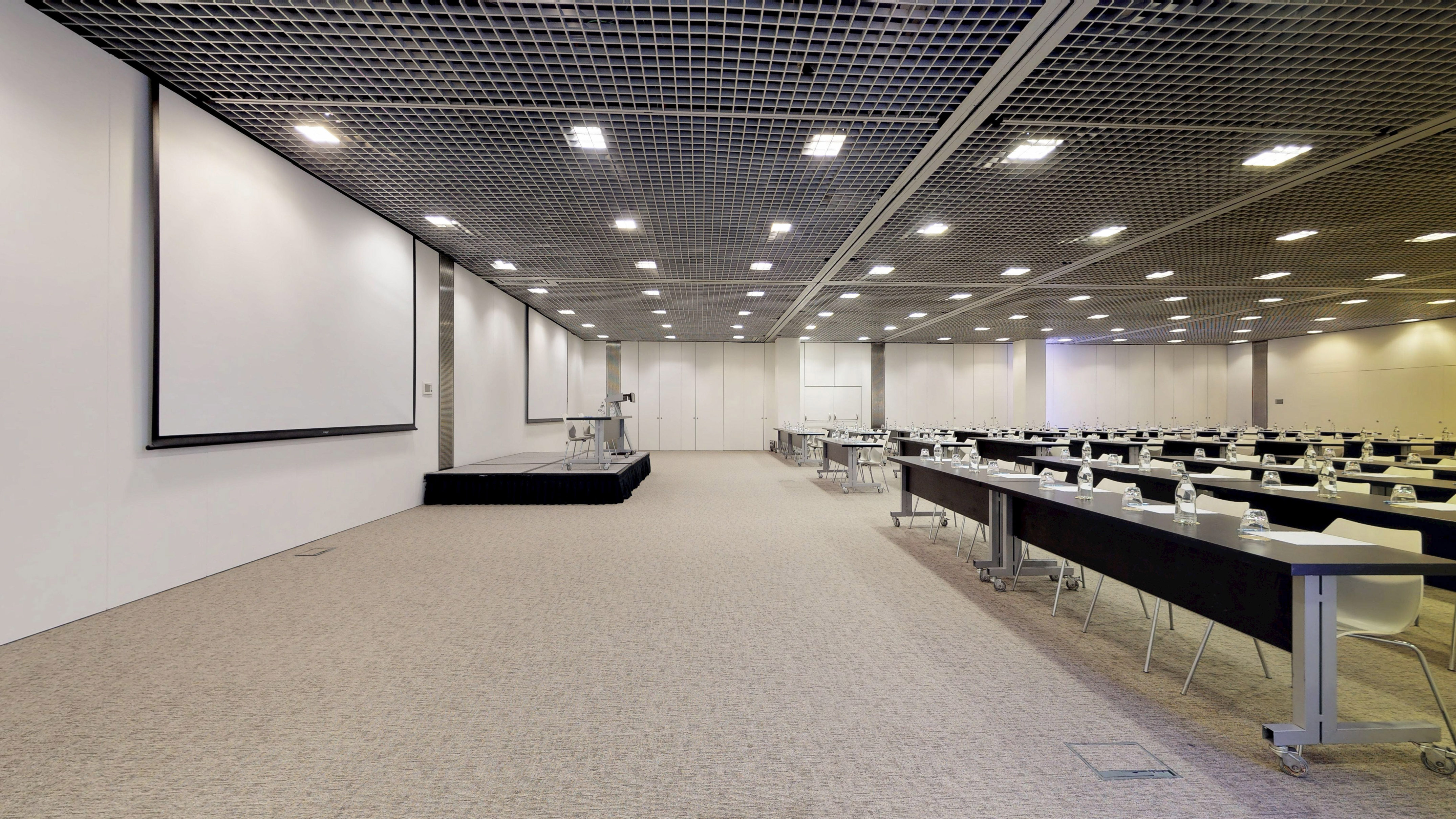Modern conference room with stage, screen, and rows of tables for meetings.