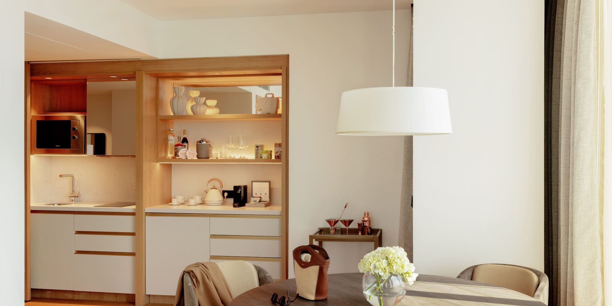 Bright hotel suite interior featuring a modern kitchenette and round dining table.