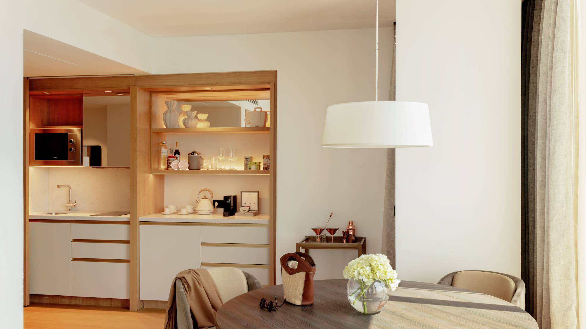 Bright hotel suite interior featuring a modern kitchenette and round dining table.
