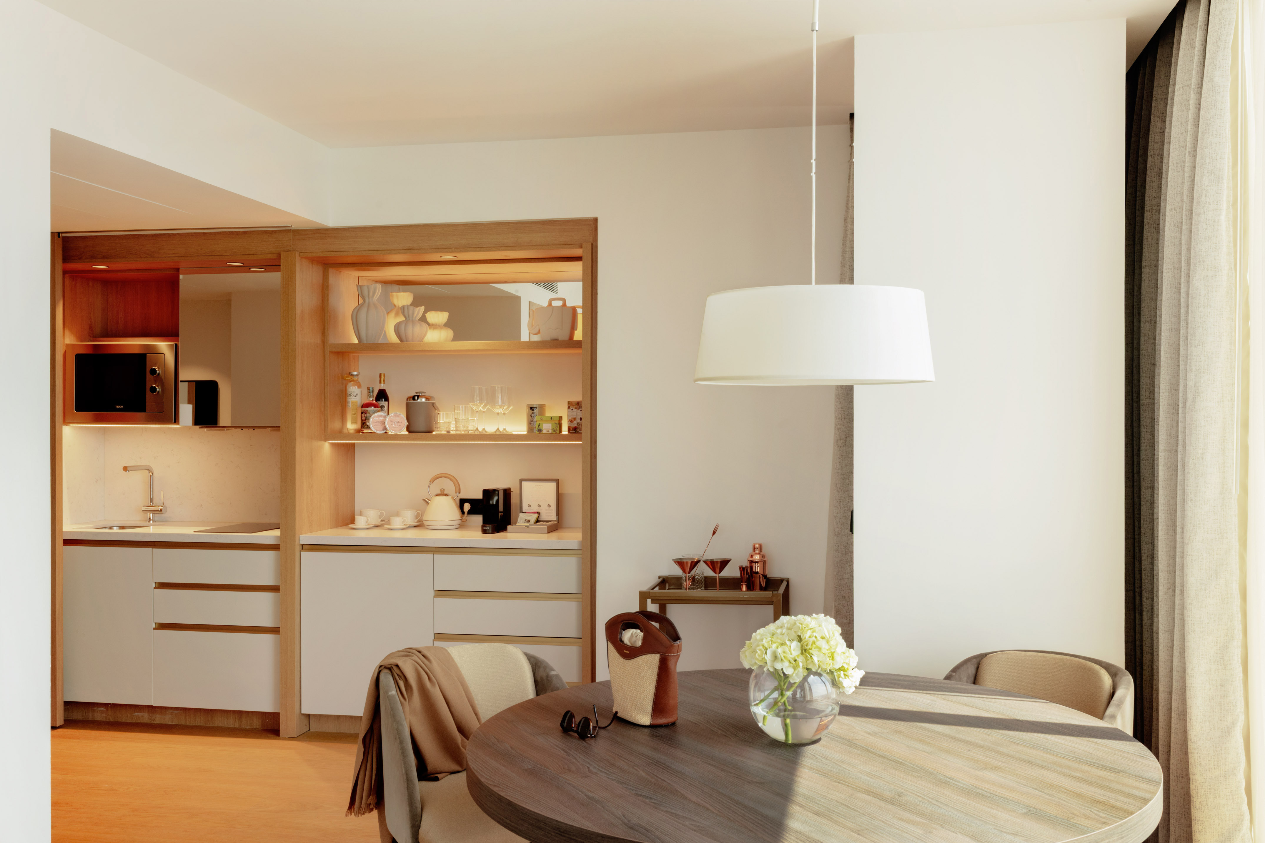 Bright hotel suite interior featuring a modern kitchenette and round dining table.