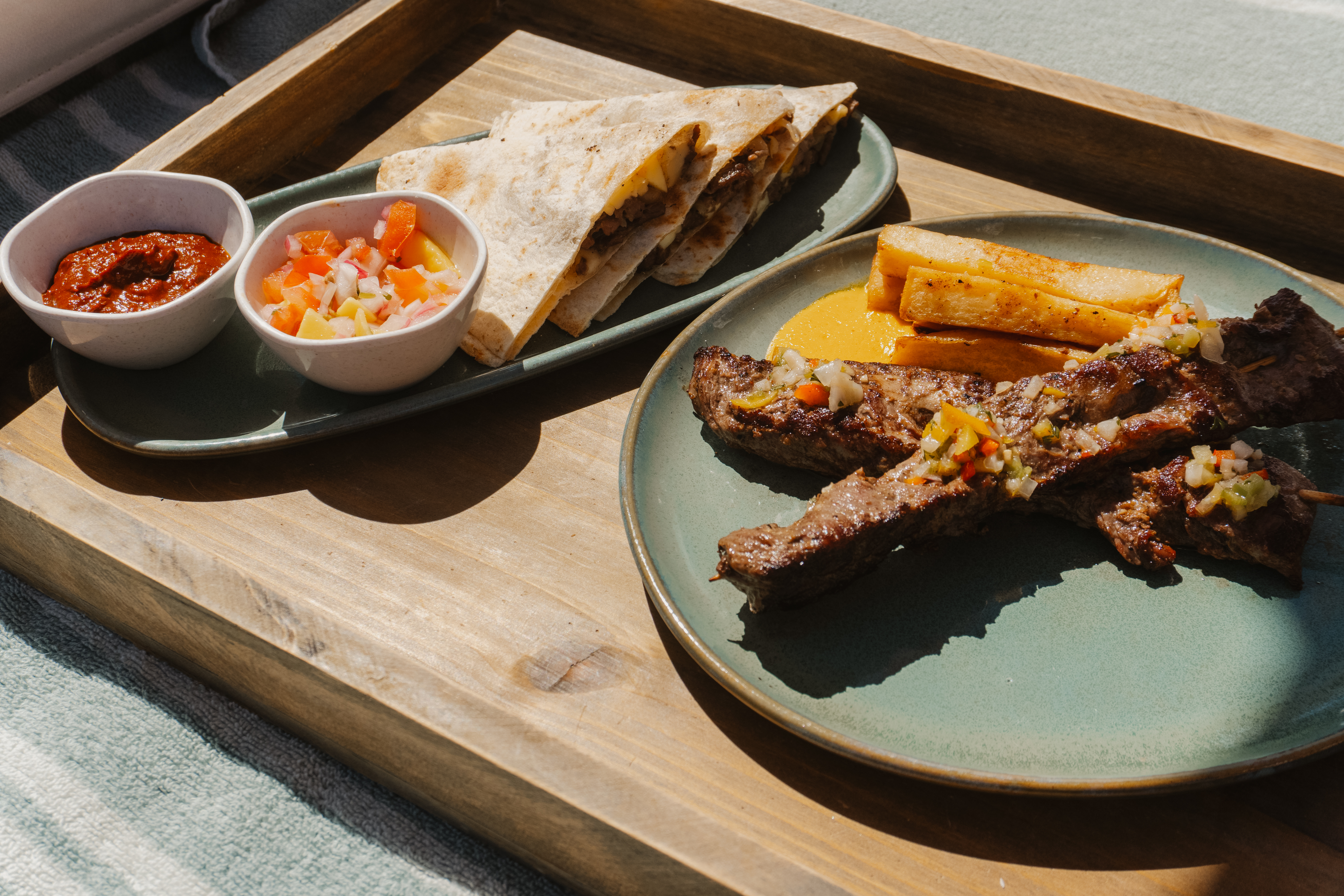 Quesadillas, steak skewers, french fries, salsa, and pico de gallo on a wooden tray.