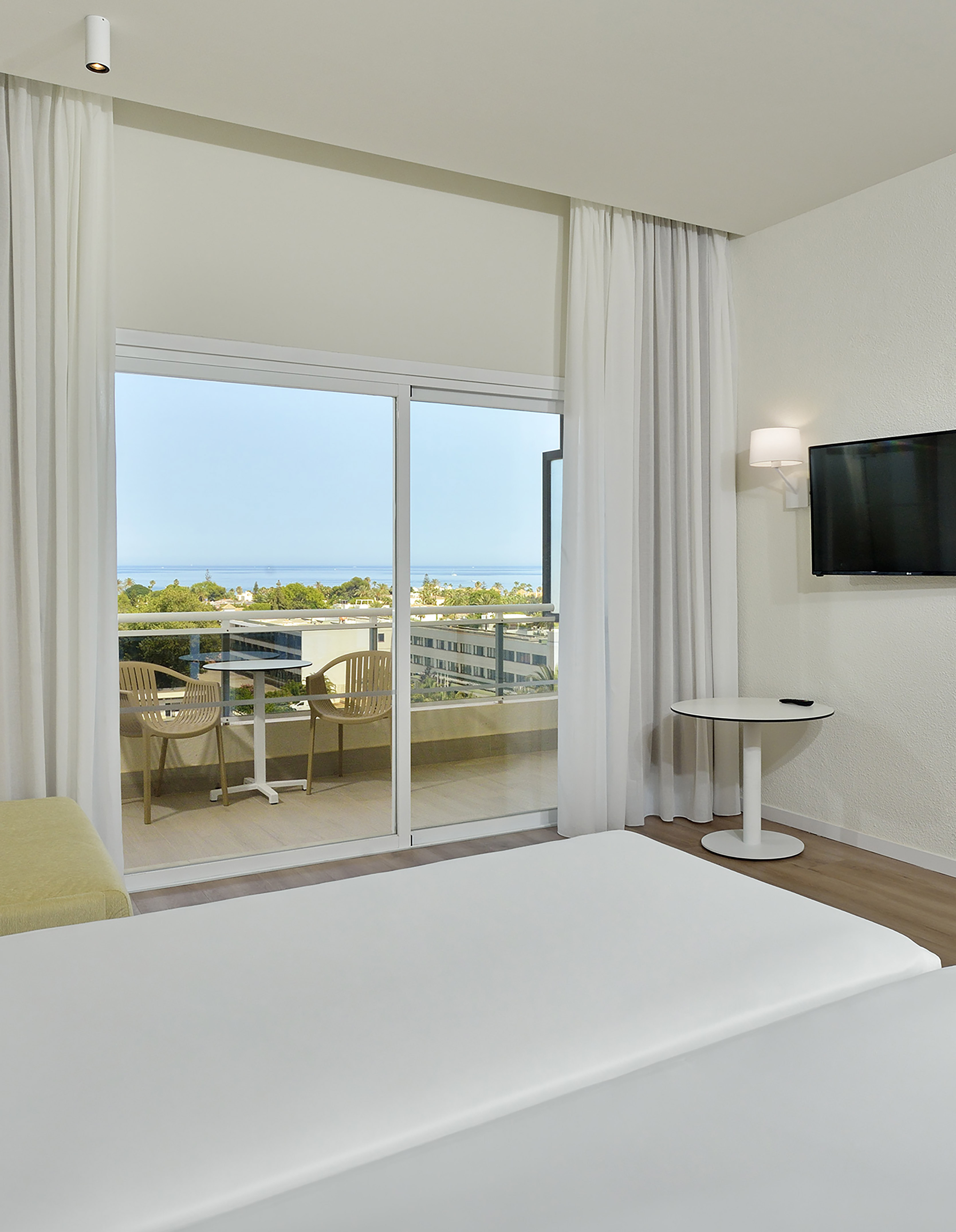 Modern hotel room with ocean view balcony, white bed, and minimalist design.