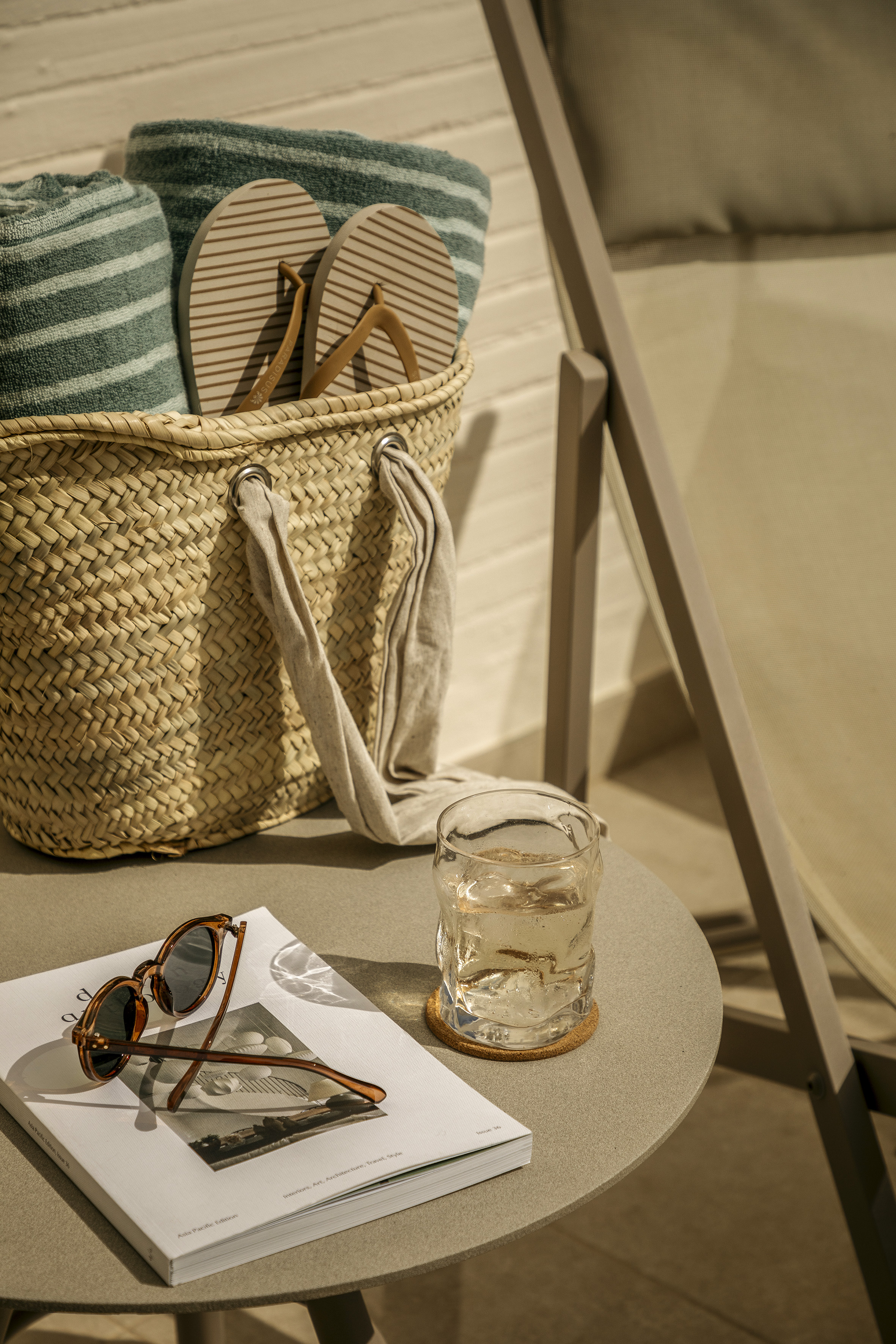 Beach vacation items: straw bag, green towels, flip-flops, sunglasses, iced drink.