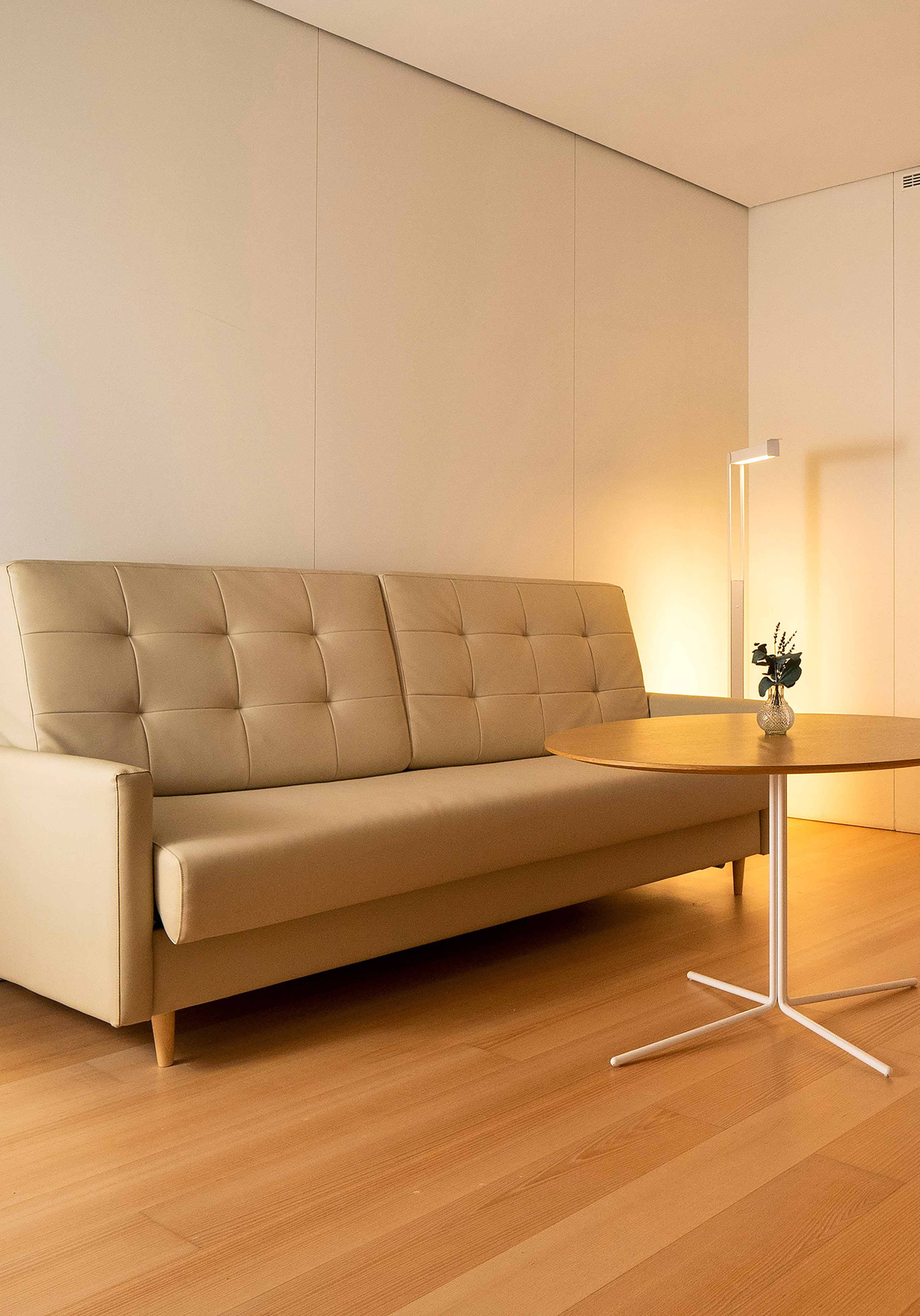 Neutral living room with beige tufted sofa, round wooden table, and warm lighting.