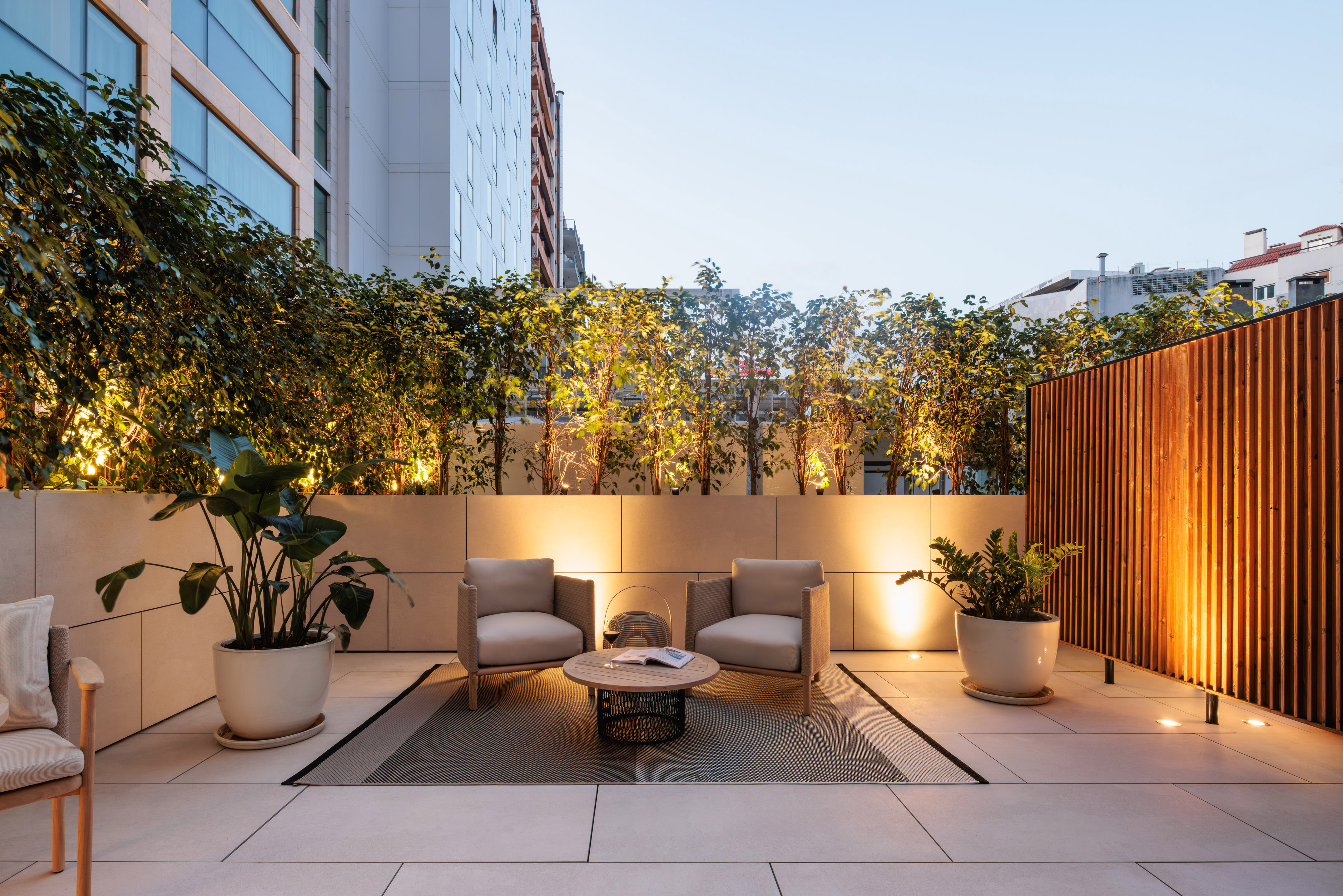 Modern outdoor terrace with lounge chairs, potted plants, and warm evening lighting.