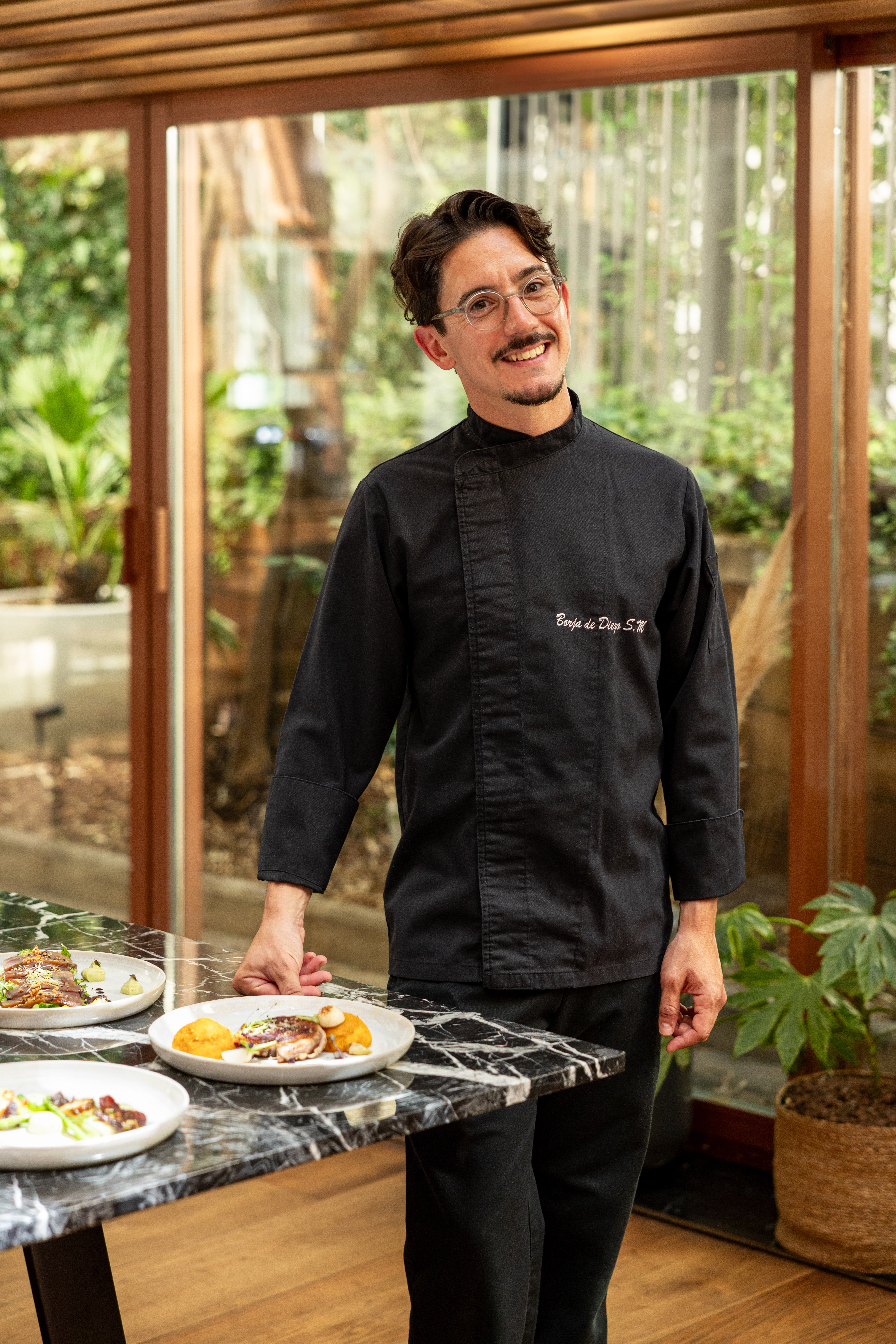 Chef Borja de Diego S.M. presenting gourmet dishes in his modern restaurant.