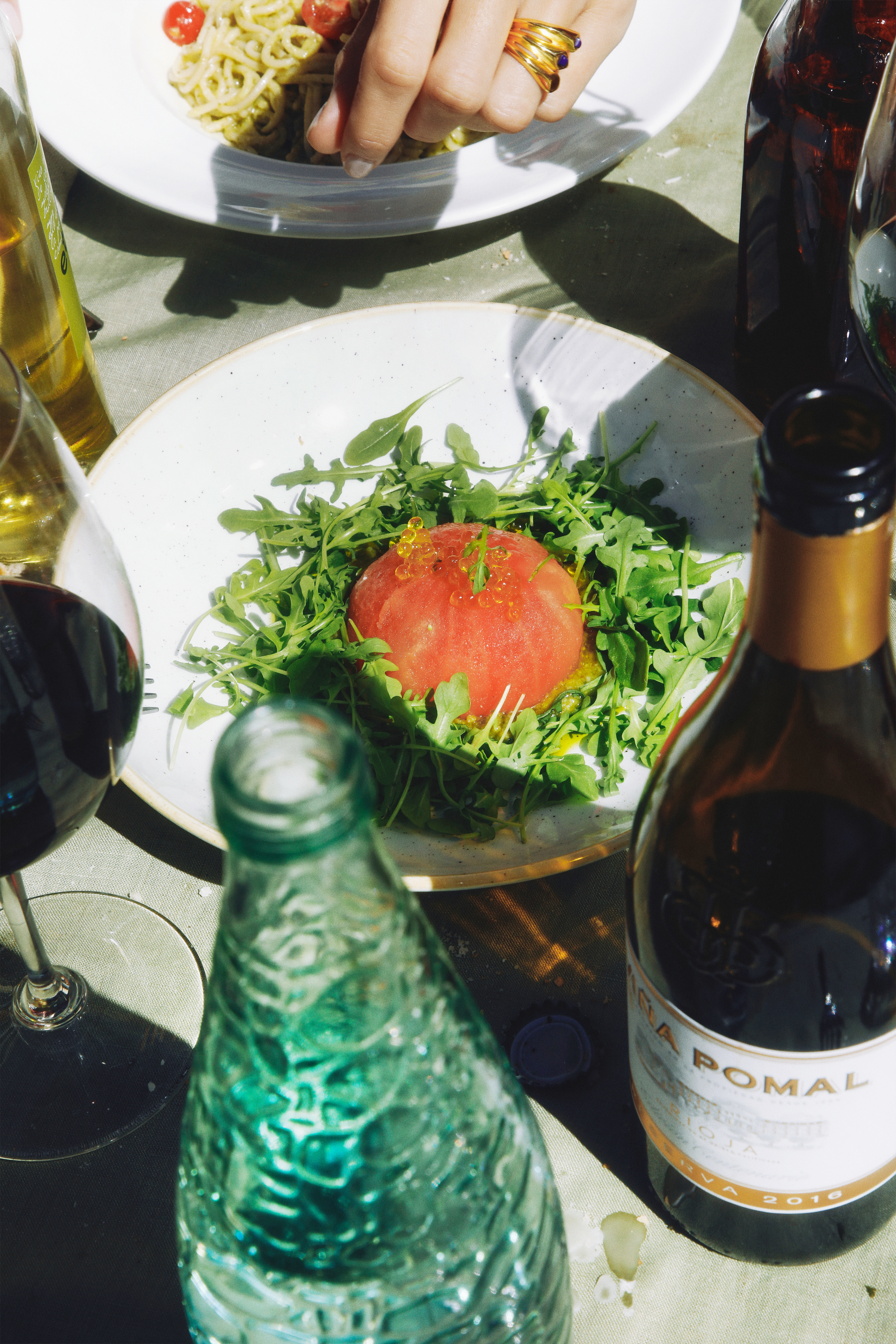 Fresh tomato & arugula salad, pesto pasta, red wine, sunlit outdoor dining.