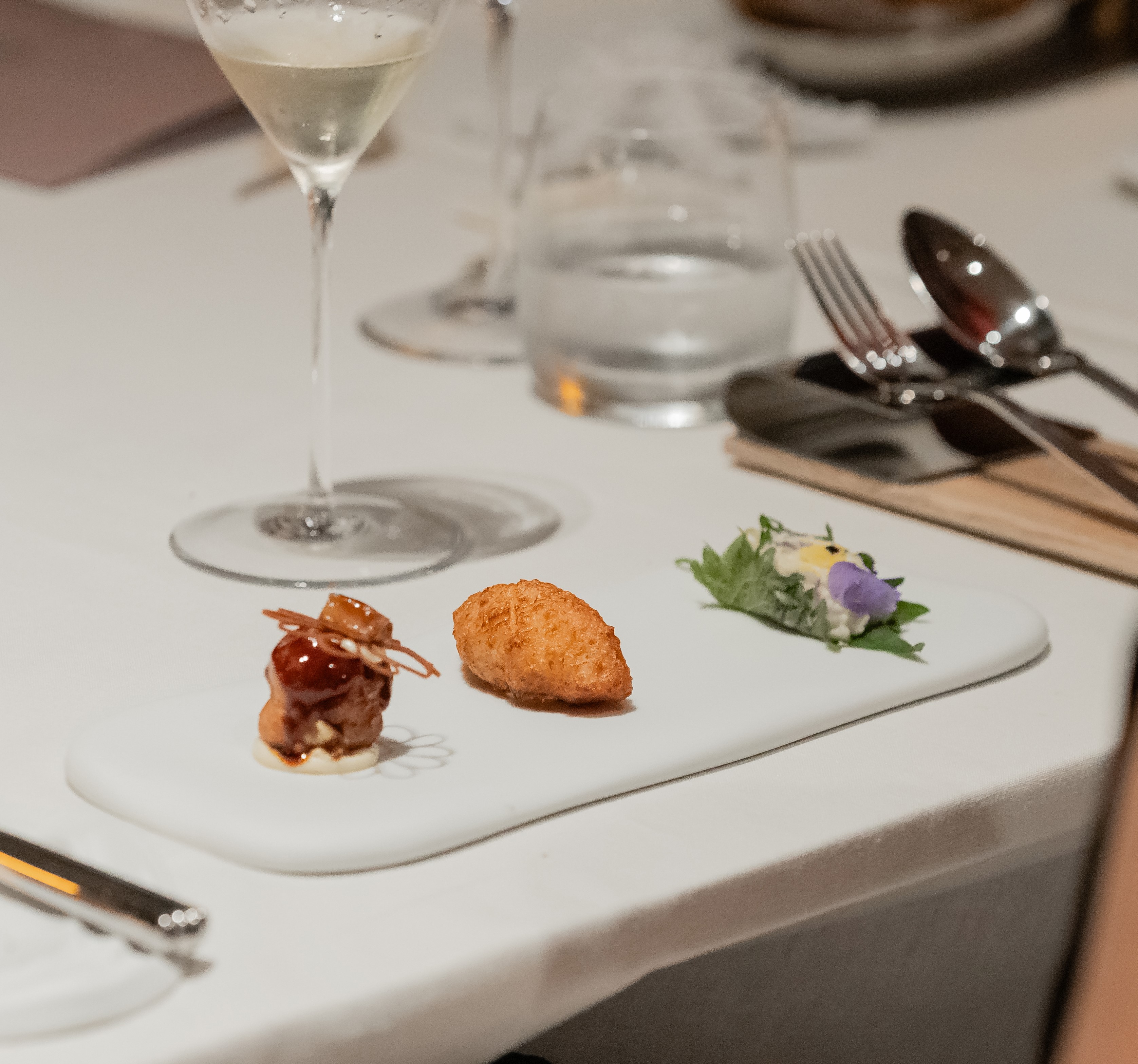 Gourmet amuse-bouche: glazed bite, croquette, floral dish, with wine.