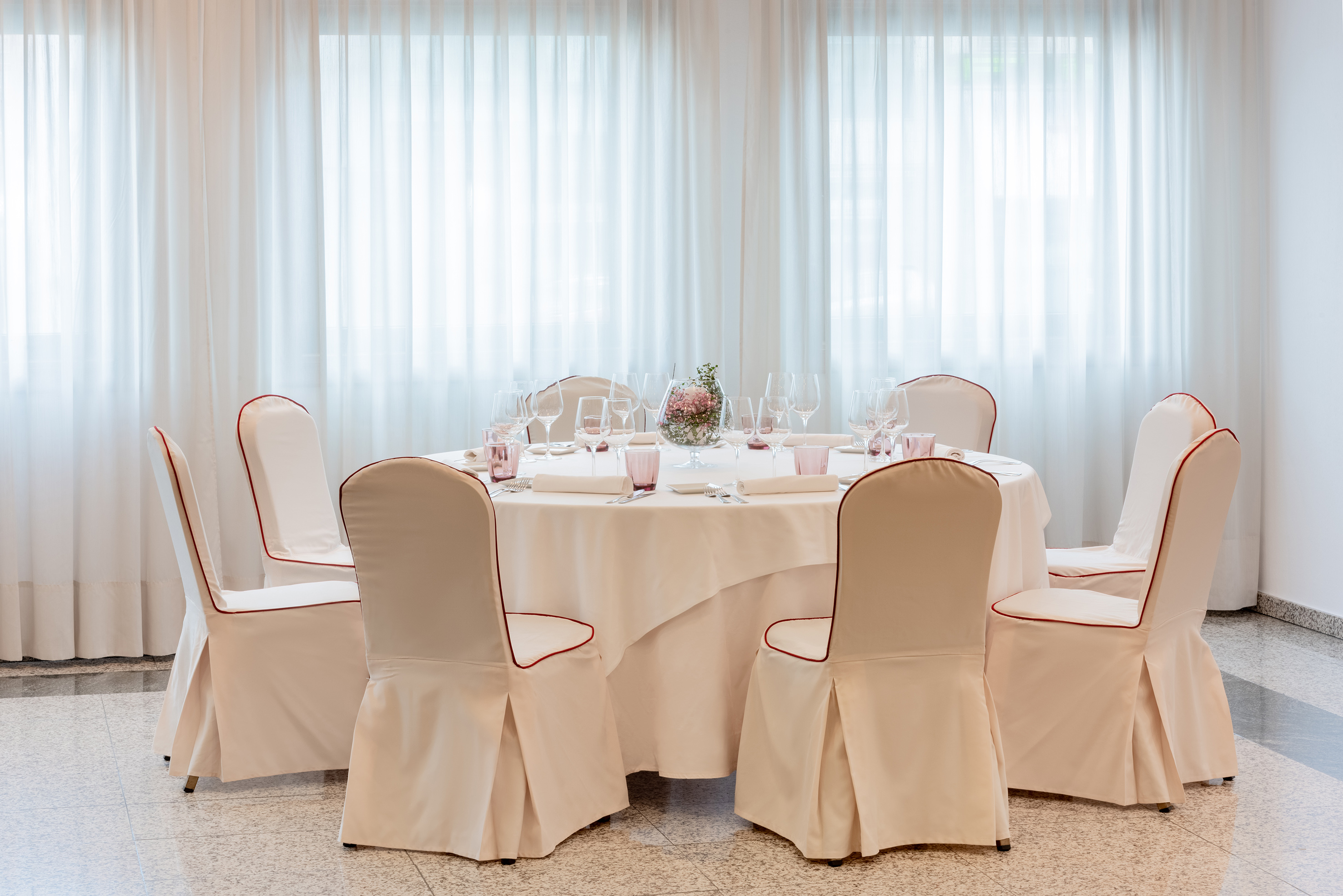 Banquet table set with white chairs, red piping, and floral centerpiece.