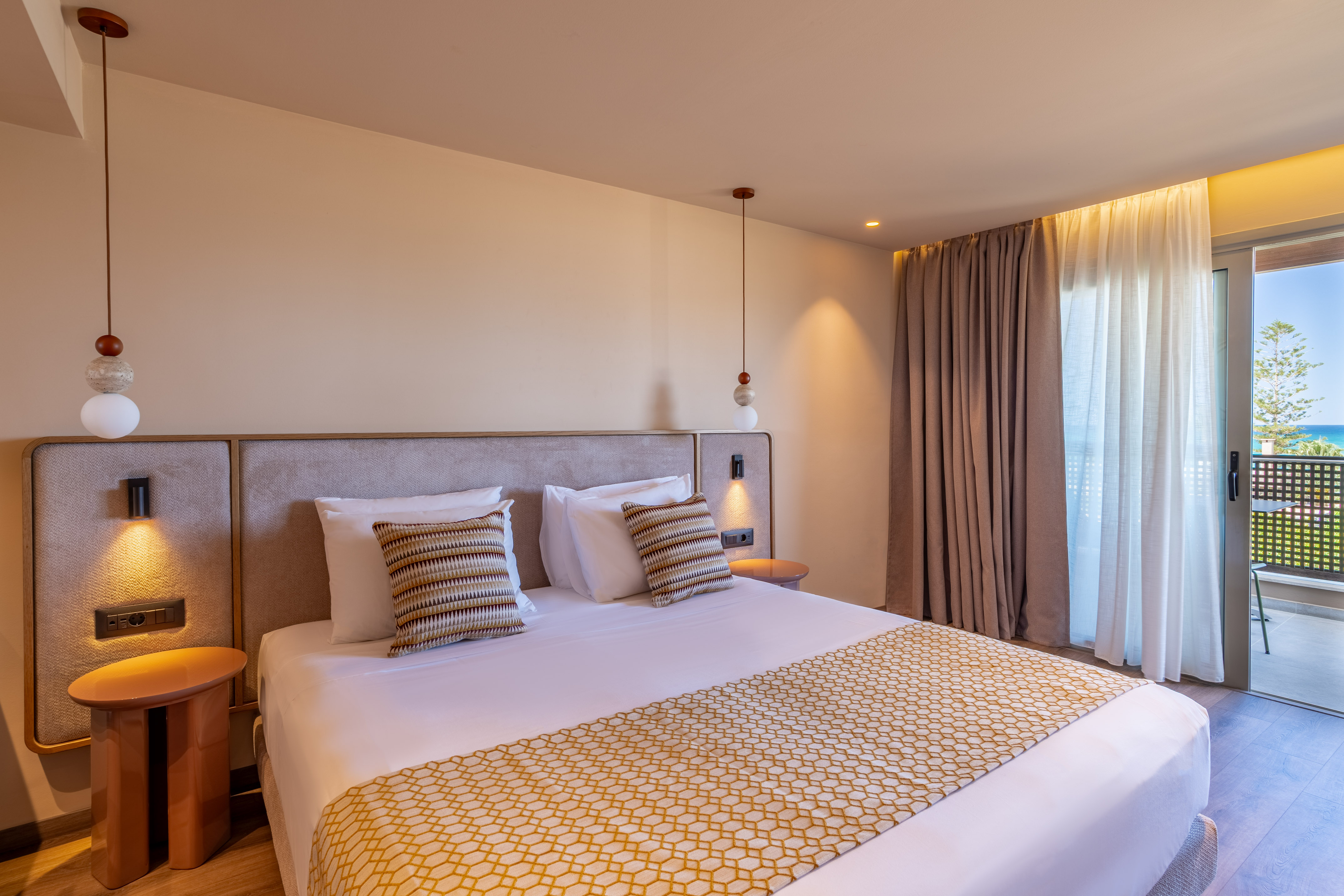 Modern hotel room with bed, patterned runner, and balcony ocean view.