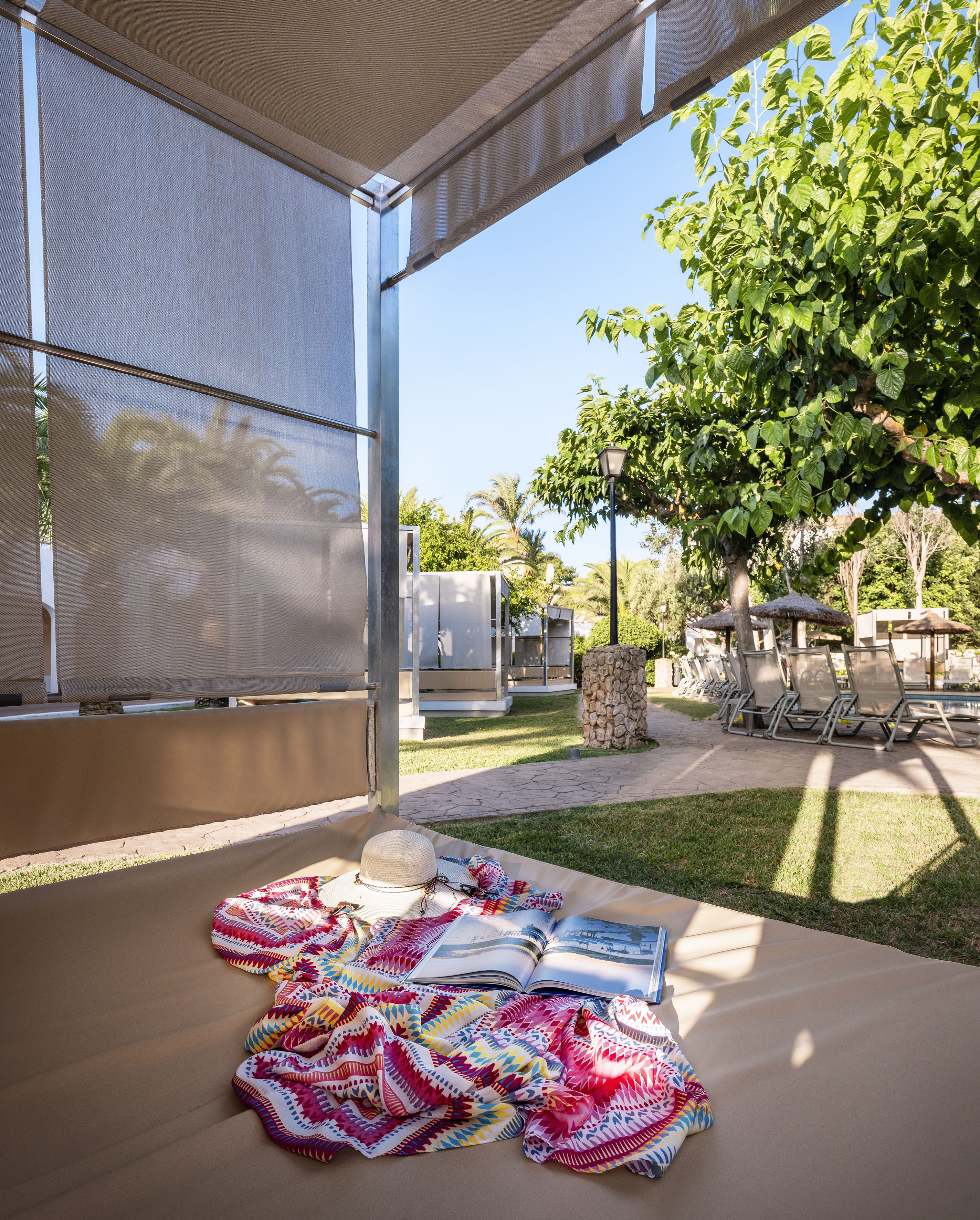 Outdoor resort cabana with hat, colorful sarong, book, and lush garden.
