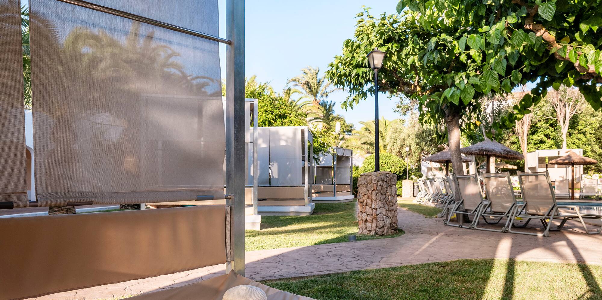 Outdoor resort cabana with hat, colorful sarong, book, and lush garden.