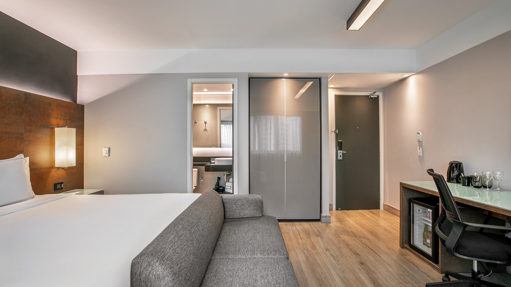 Quarto de hotel moderno com cama de casal, sofá cinza, escrivaninha e banheiro. - Deluxe Room Queen - Meliá Ibirapuera, São Paulo