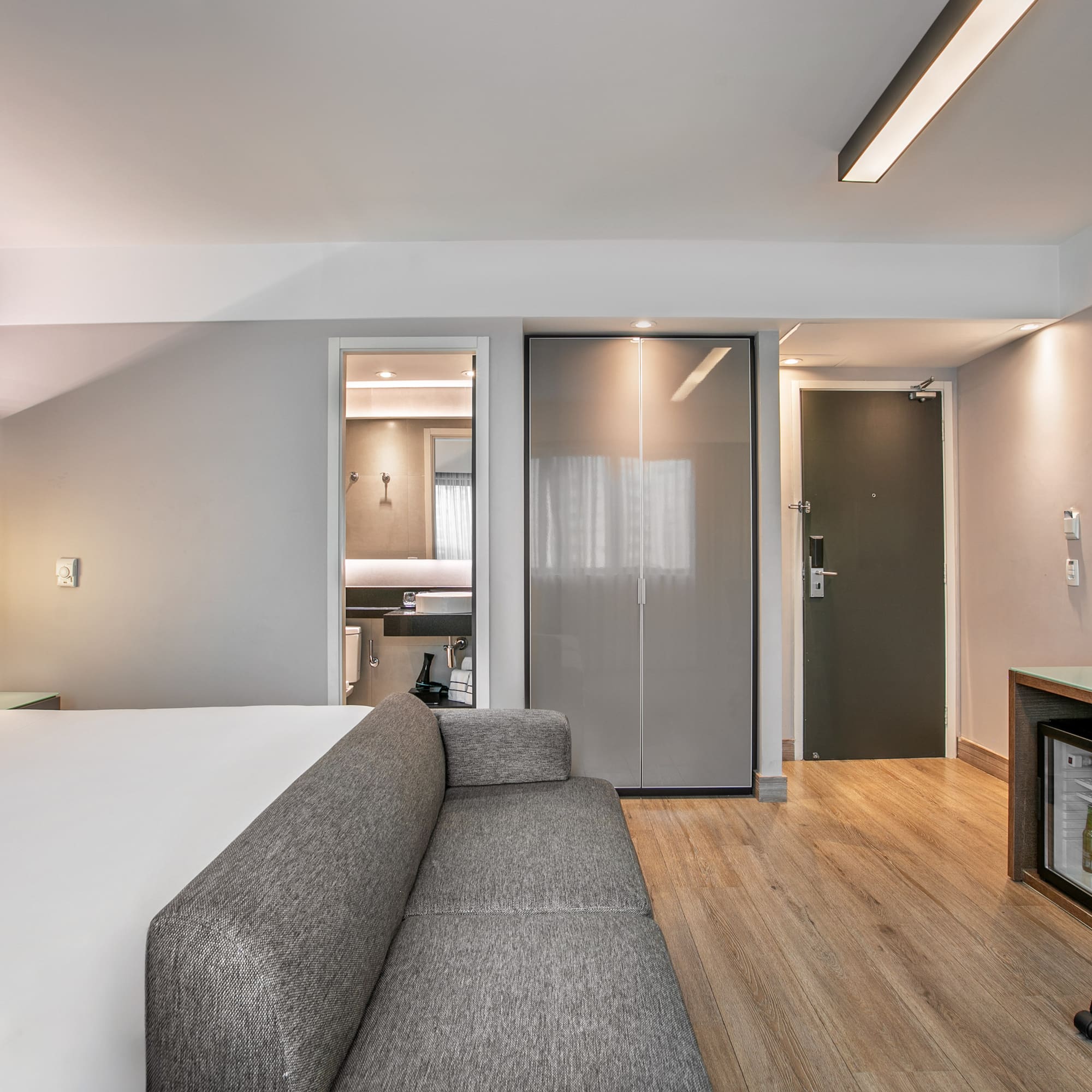 Quarto de hotel moderno com cama de casal, sofá cinza, escrivaninha e banheiro. - Deluxe Room Queen - Meliá Ibirapuera, São Paulo