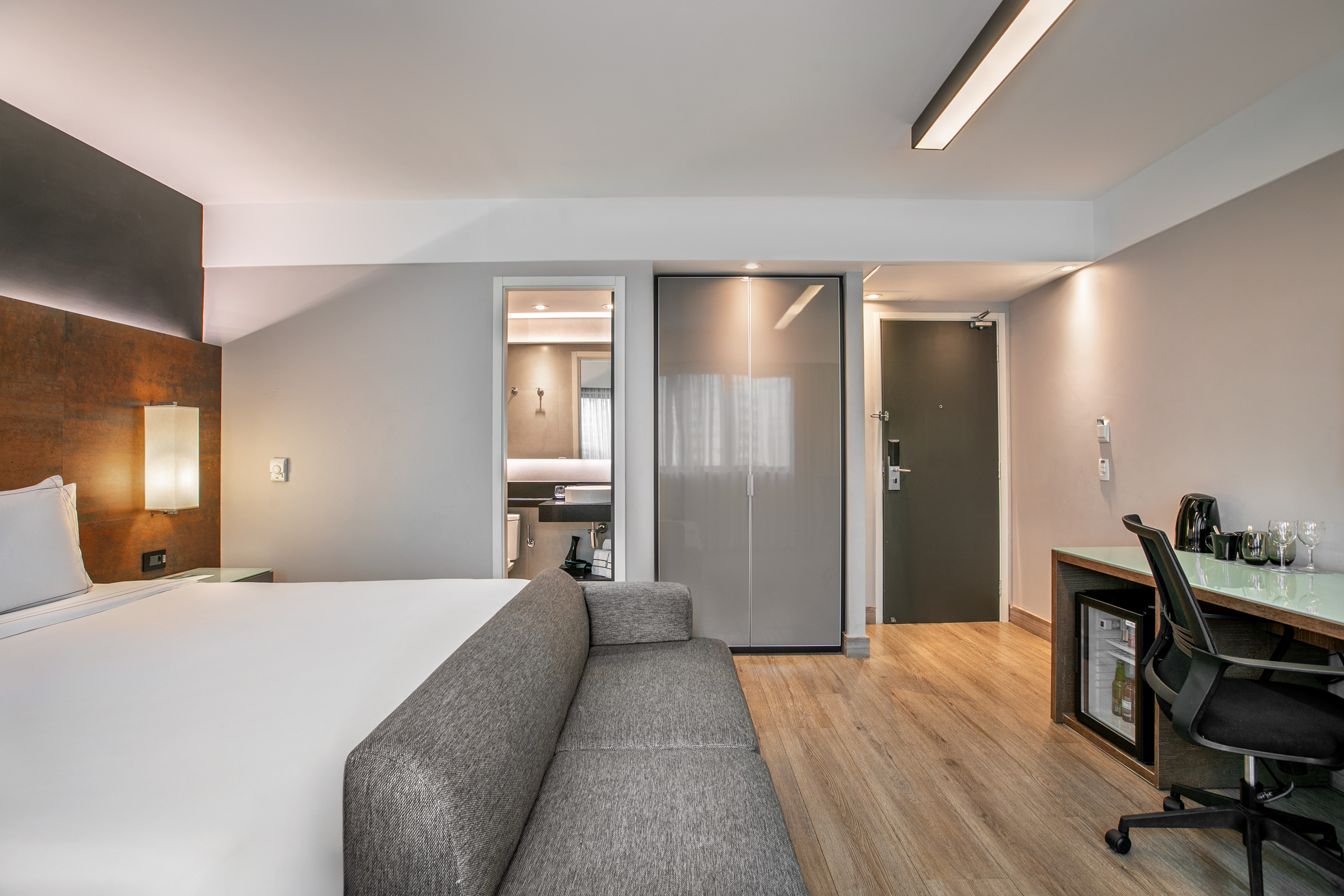Quarto de hotel moderno com cama de casal, sofá cinza, escrivaninha e banheiro. - Deluxe Room Queen - Meliá Ibirapuera, São Paulo
