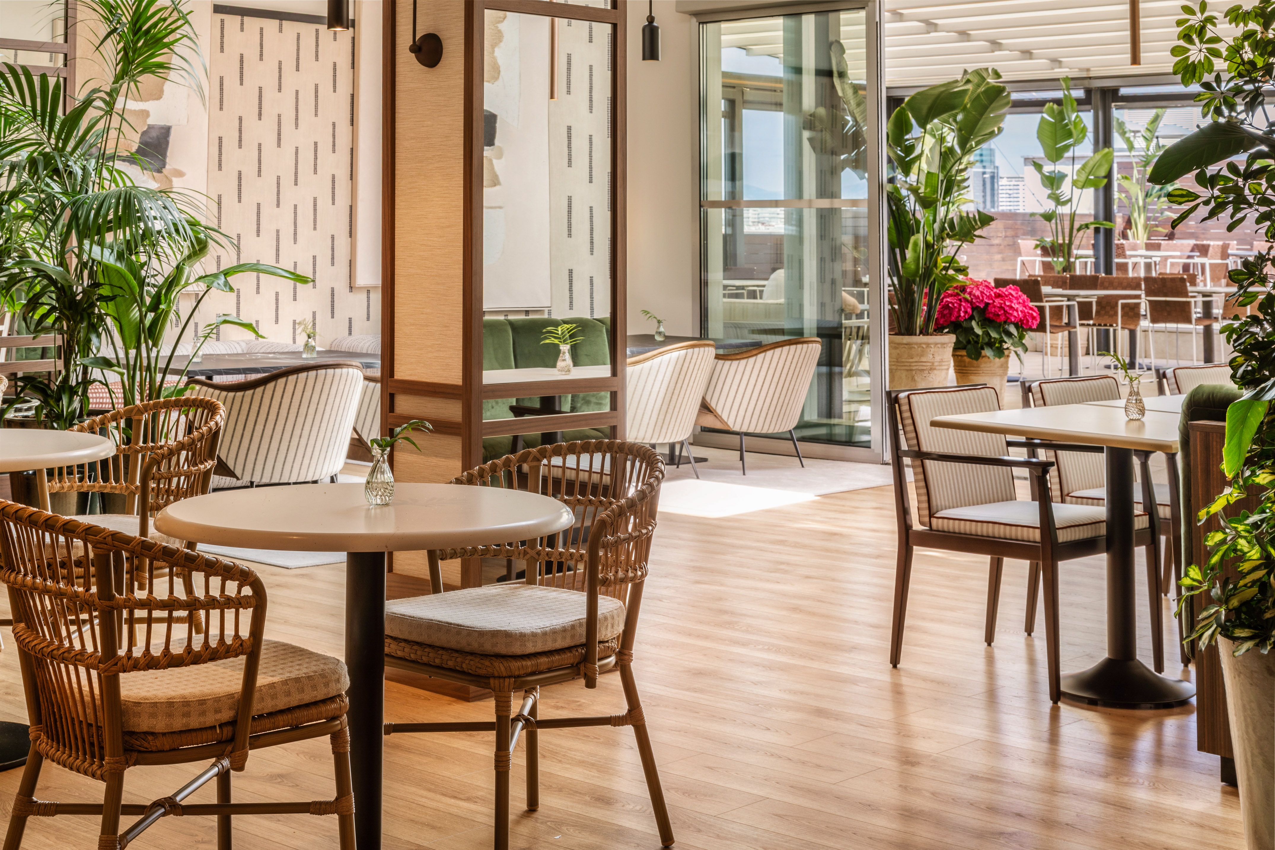 Restaurante luminoso con sillas de ratán, plantas y terraza exterior.