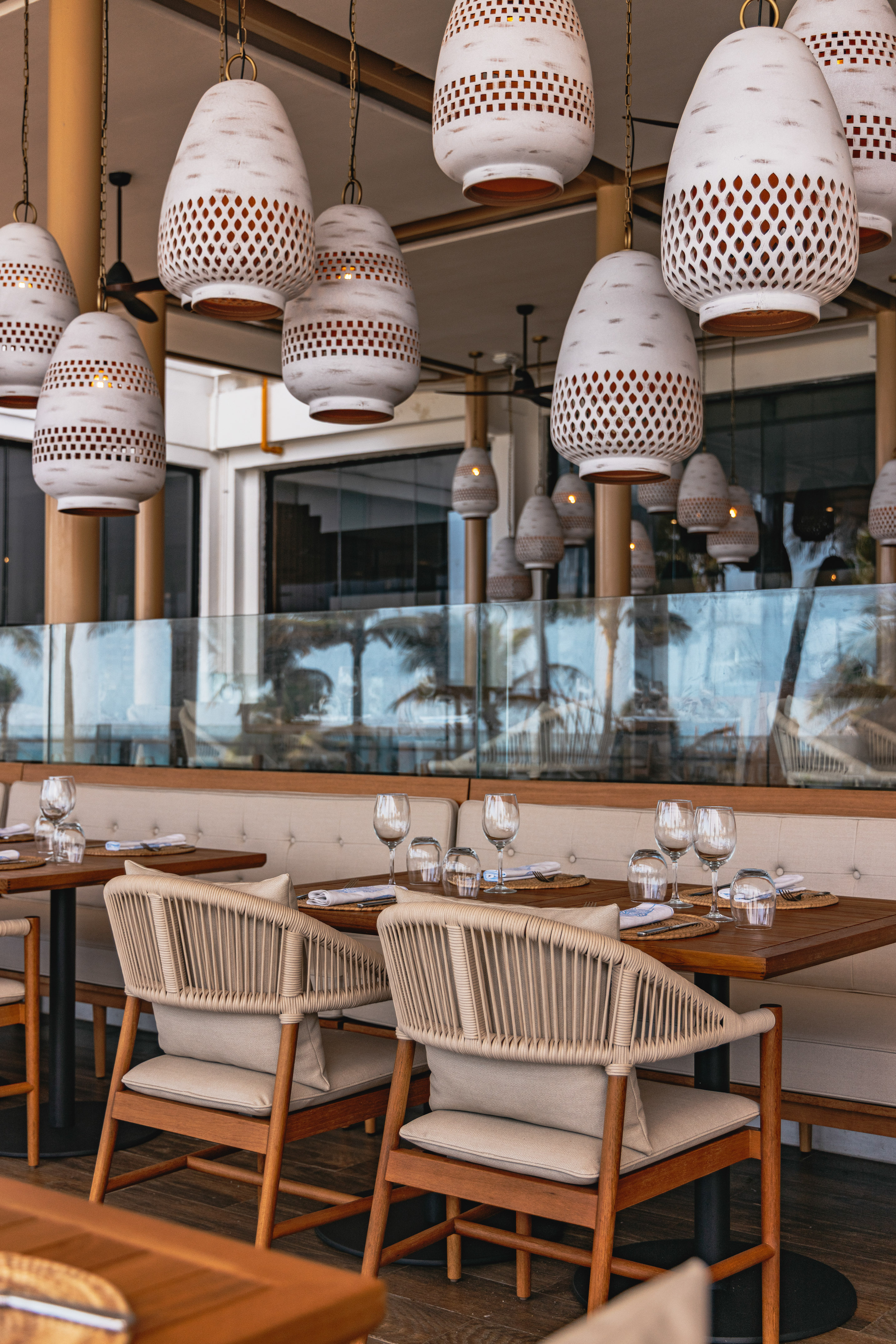 Resort dining patio with woven chairs, set tables, and decorative pendant lights.