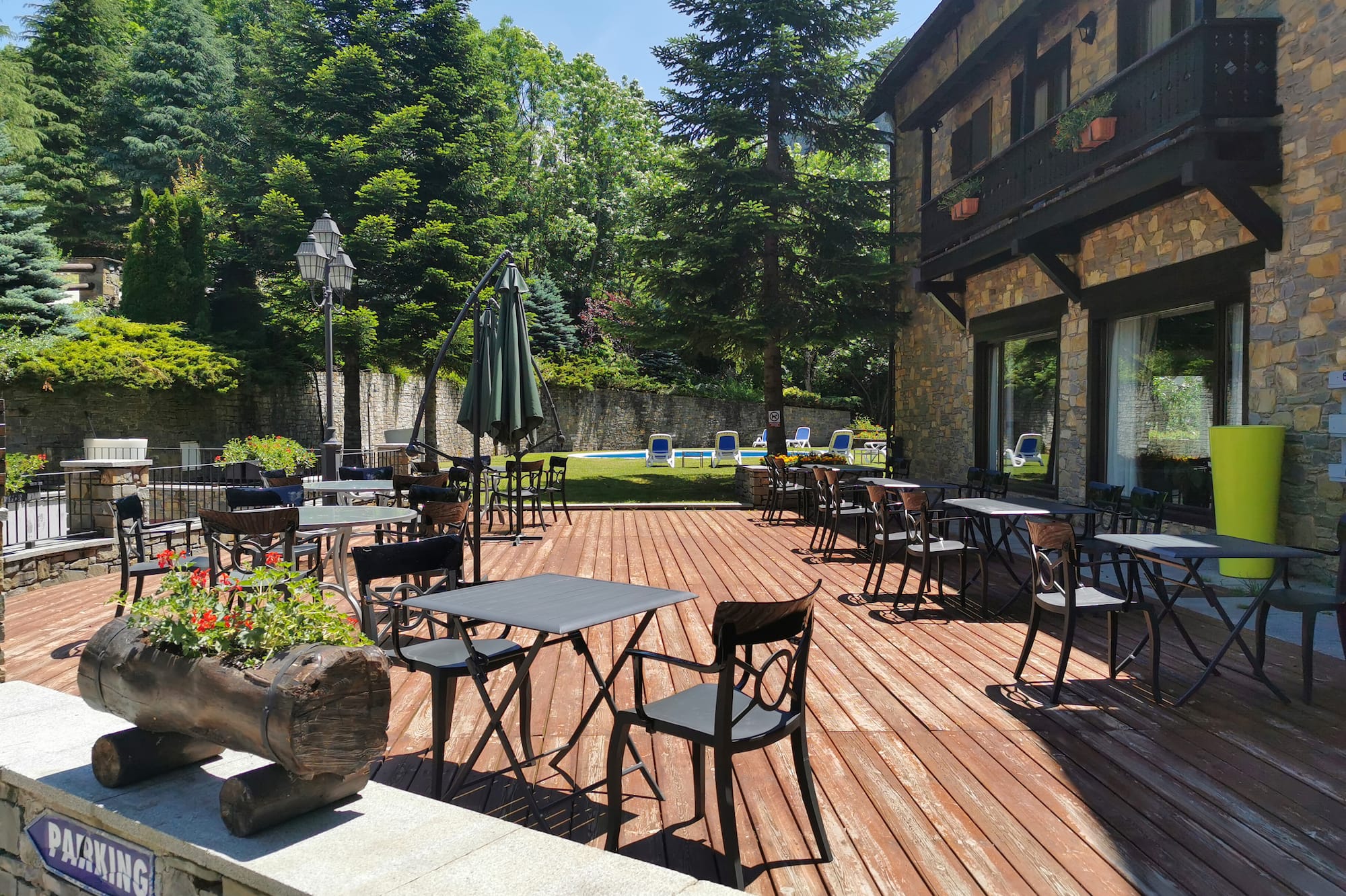 Terraza exterior de hotel con mesas, sillas, piscina y frondoso jardín.
