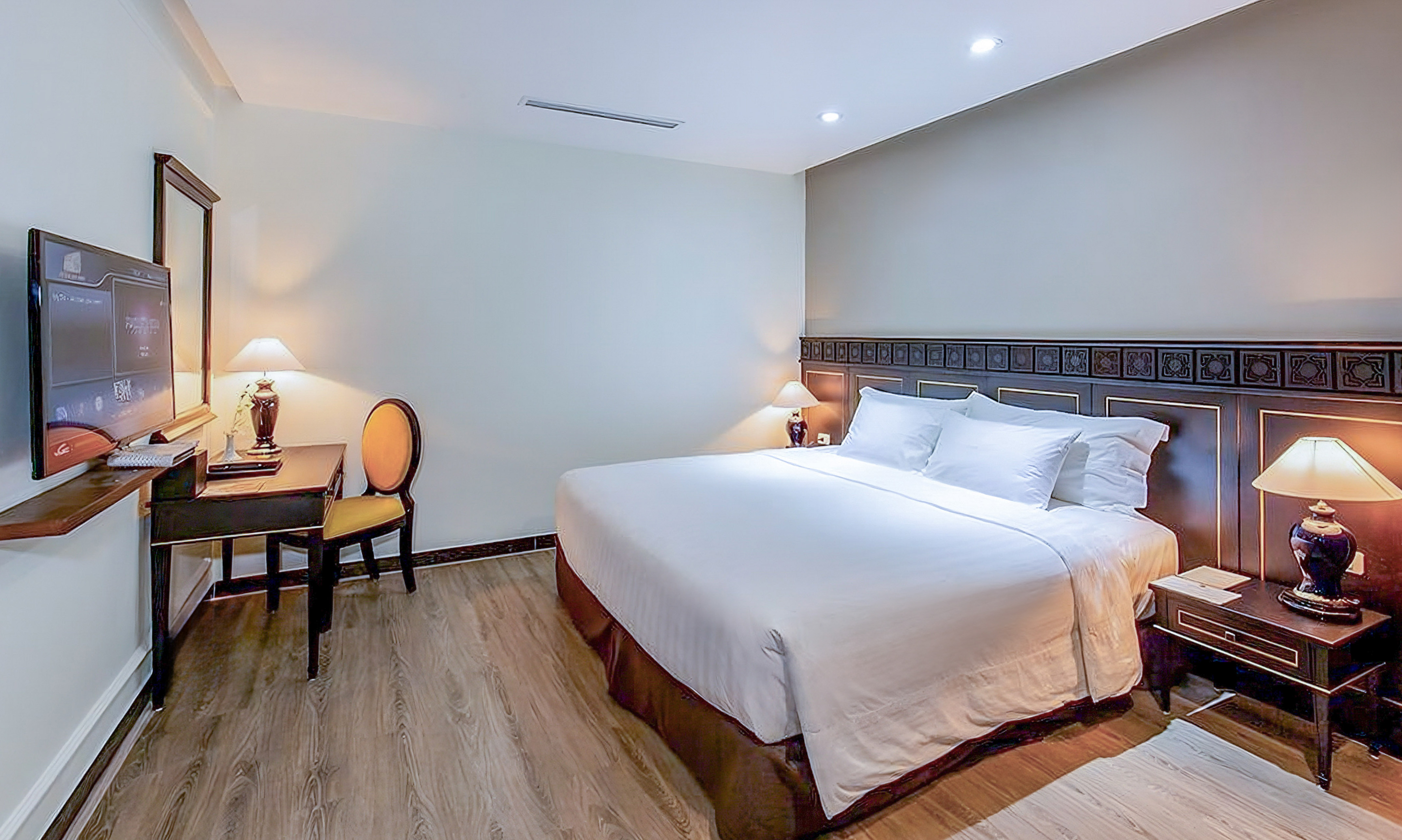 Modern hotel bedroom with white queen bed, dark wood furniture, and TV.