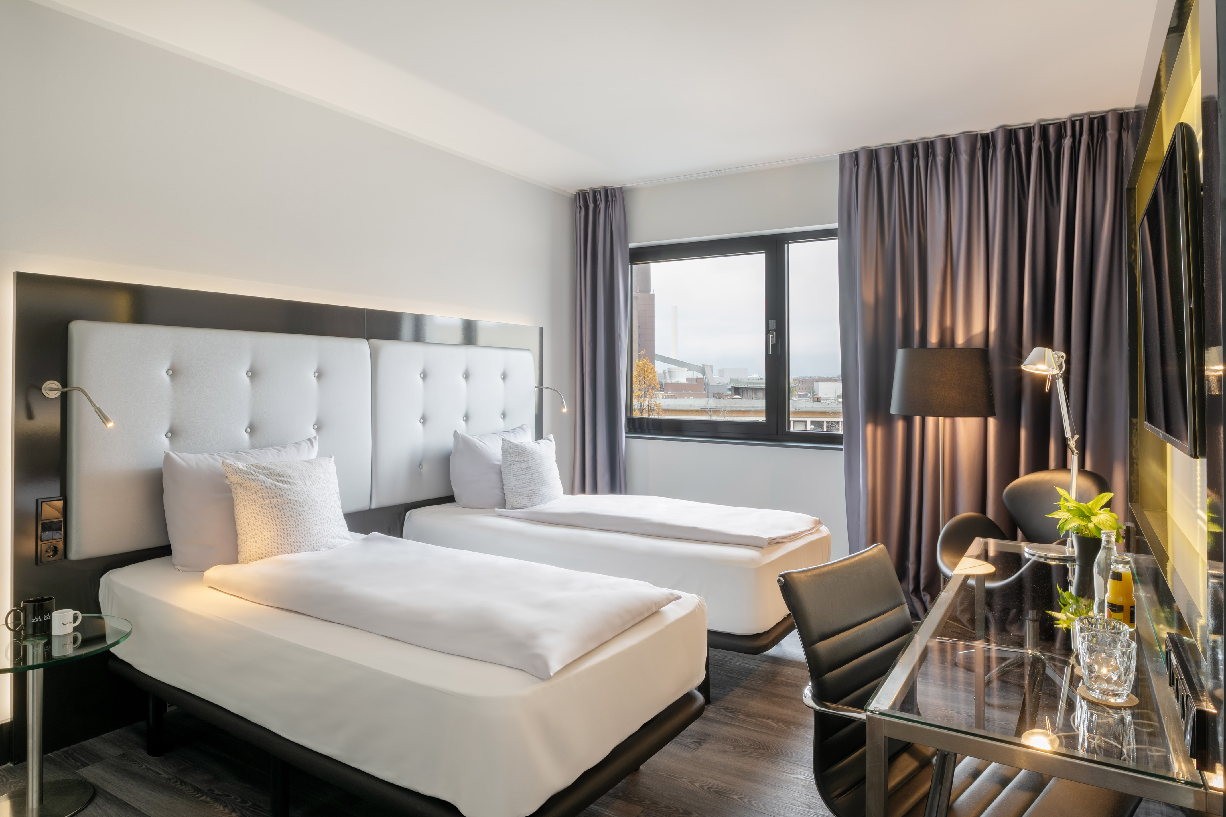 Modern hotel room with two twin beds, desk, and city view.