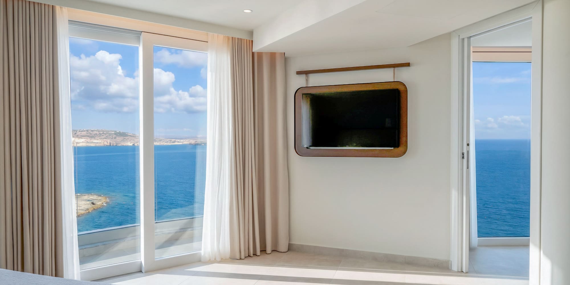 Modern bedroom with expansive ocean view, large windows, and wall-mounted TV.