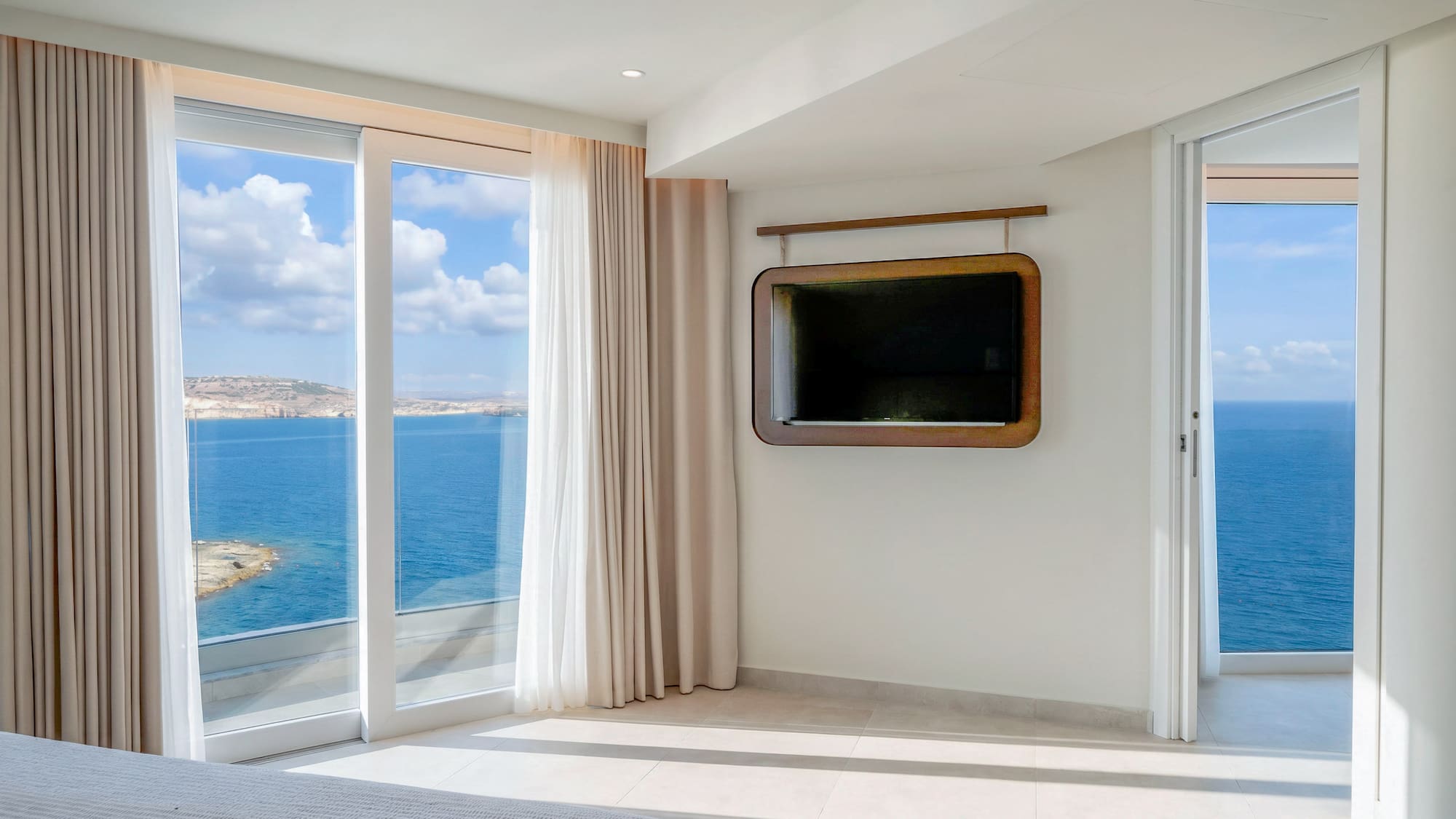 Modern bedroom with expansive ocean view, large windows, and wall-mounted TV.