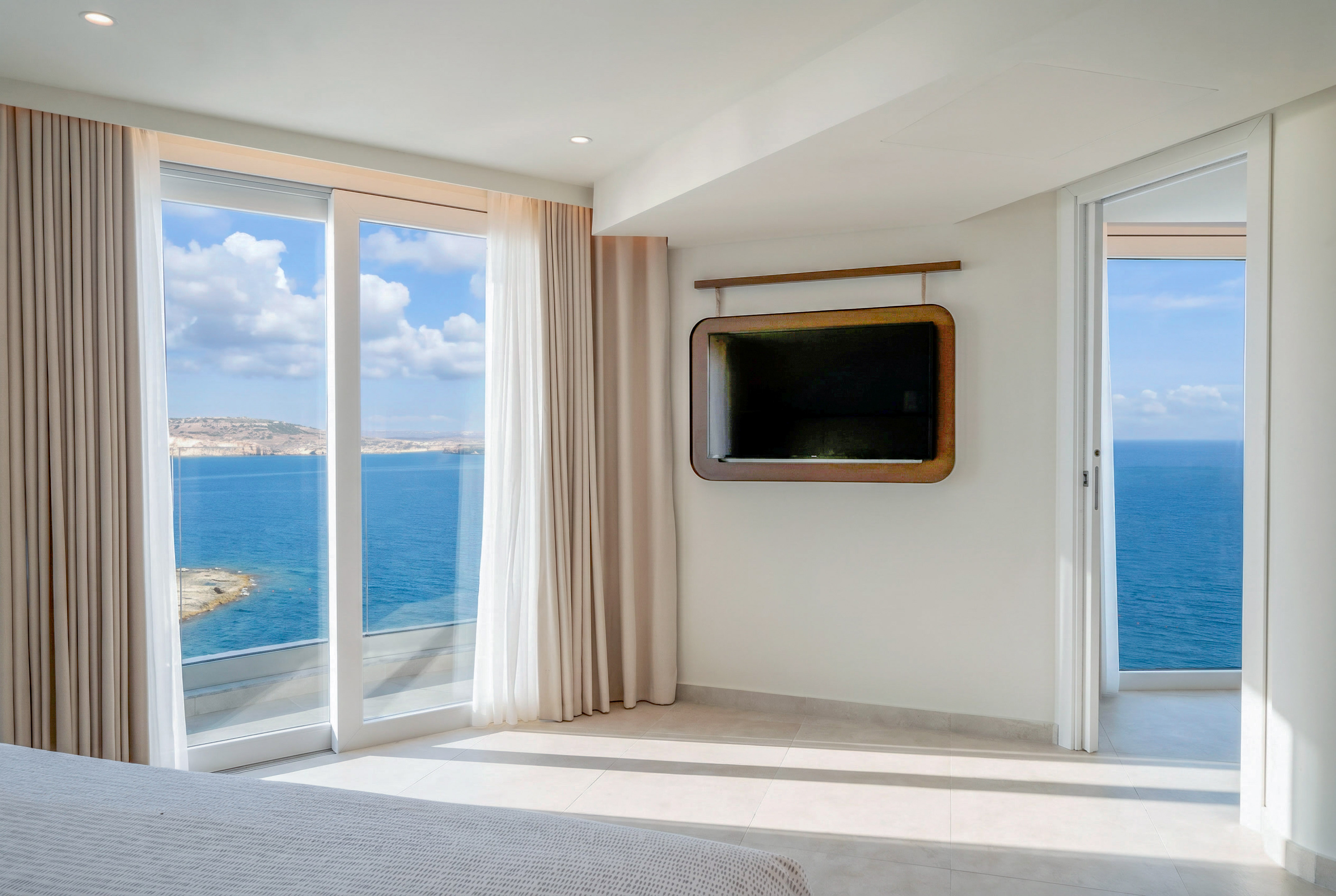 Modern bedroom with expansive ocean view, large windows, and wall-mounted TV.